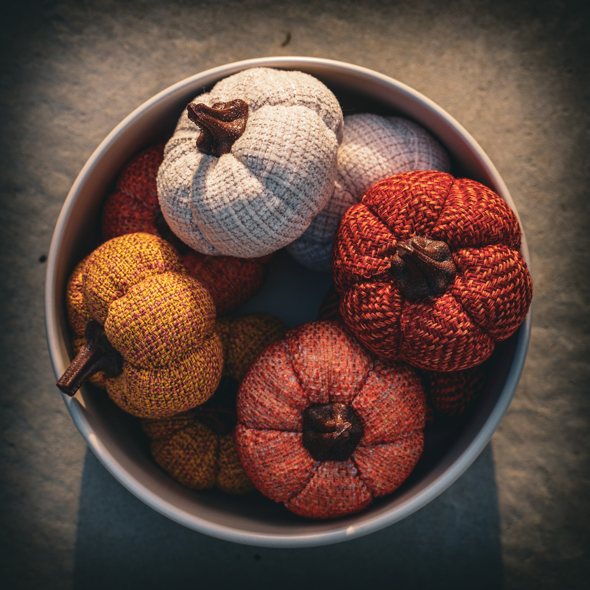 Close-up of decorative fabric pumpkins in a white bowl, with a grey background.
