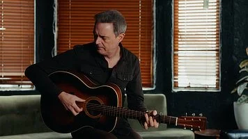 Man playing an acoustic guitar while seated indoors
