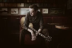 Man sitting in a dimly lit pub holding an electric guitar