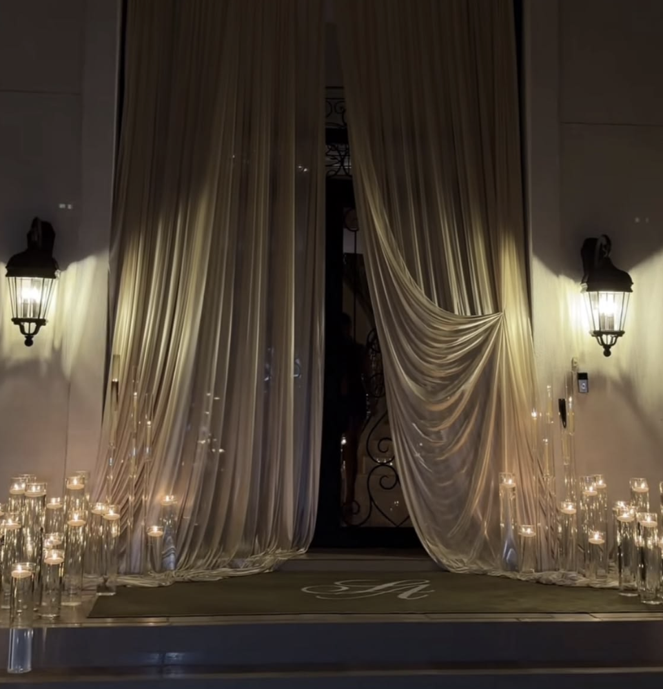 A luxurious entrance with heavy gold curtains, surrounded by lit candles in glass holders, and illuminated by wall-mounted lanterns.