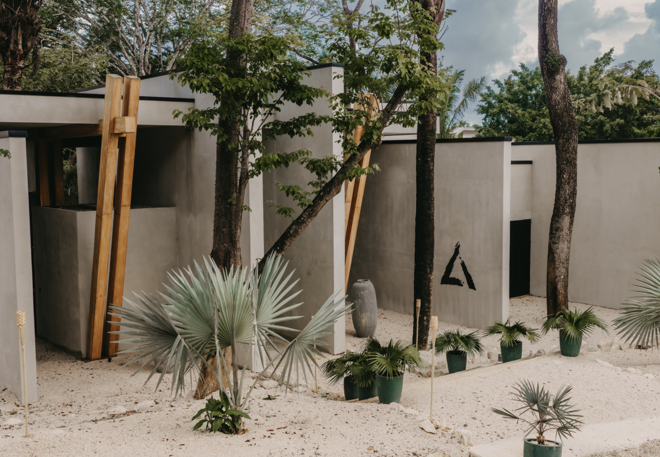 Modern outdoor building with white walls, surrounded by desert plants and trees, under a partly cloudy sky.