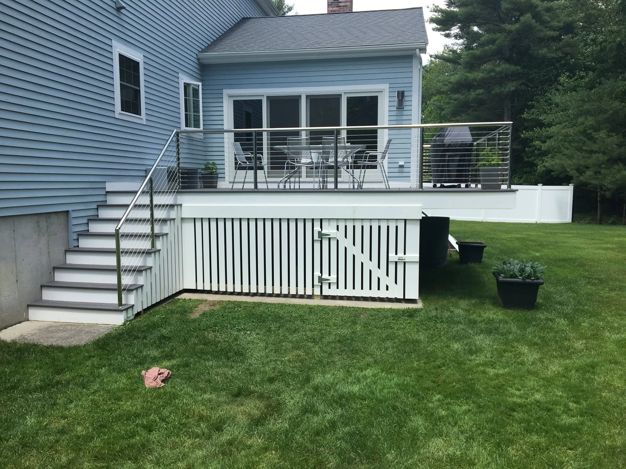 Backyard with a blue house, elevated extended deck with metal railing. Under the deck is lattice work.