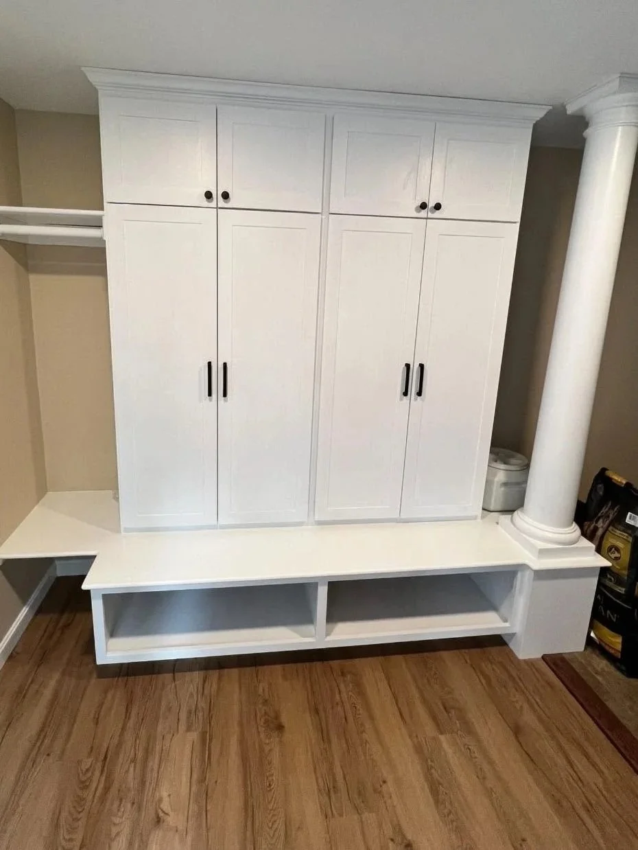 White built-in cabinetry with closed doors, black handles, and a decorative column on the right side, situated on a wooden floor in a room with beige walls.