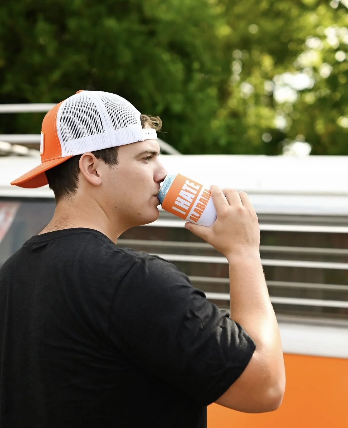 Man drinking from an orange Alabama koozie beside Nancy, orange VW bus, brand content shoot