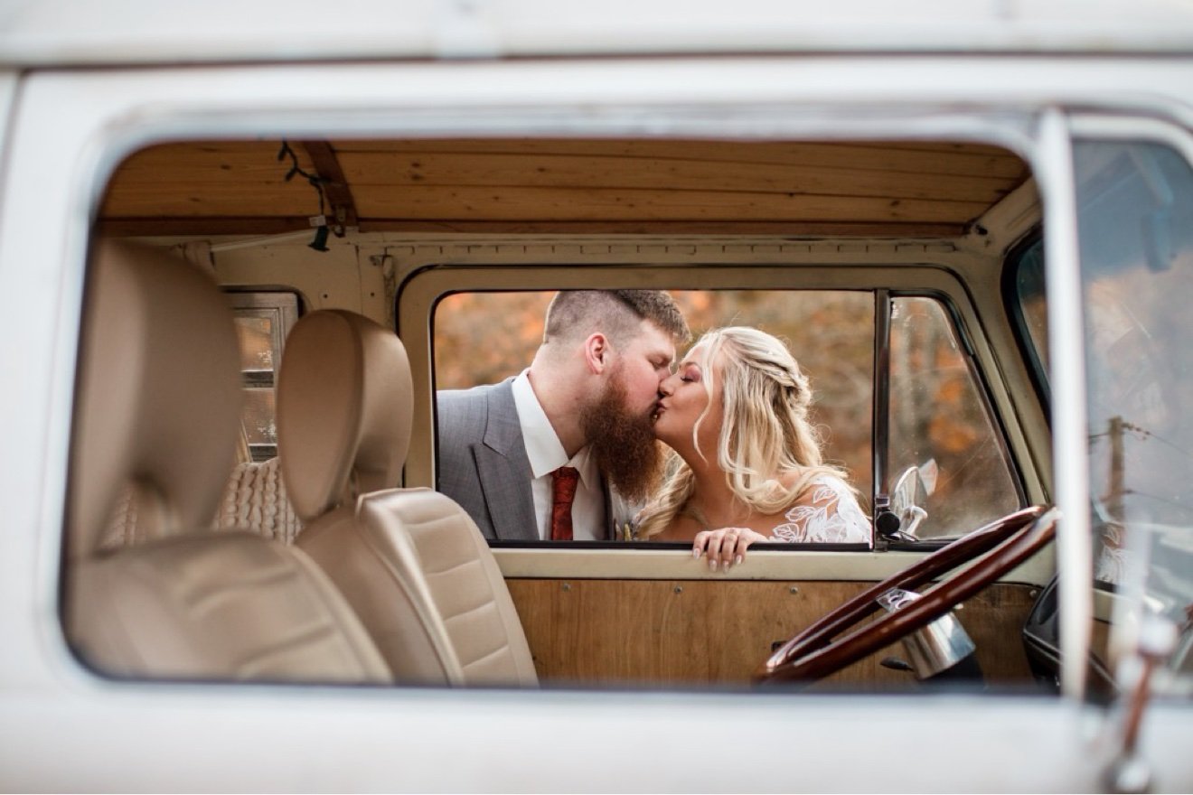 Wedding couple kissing at the window of Nancy, orange VW bus
