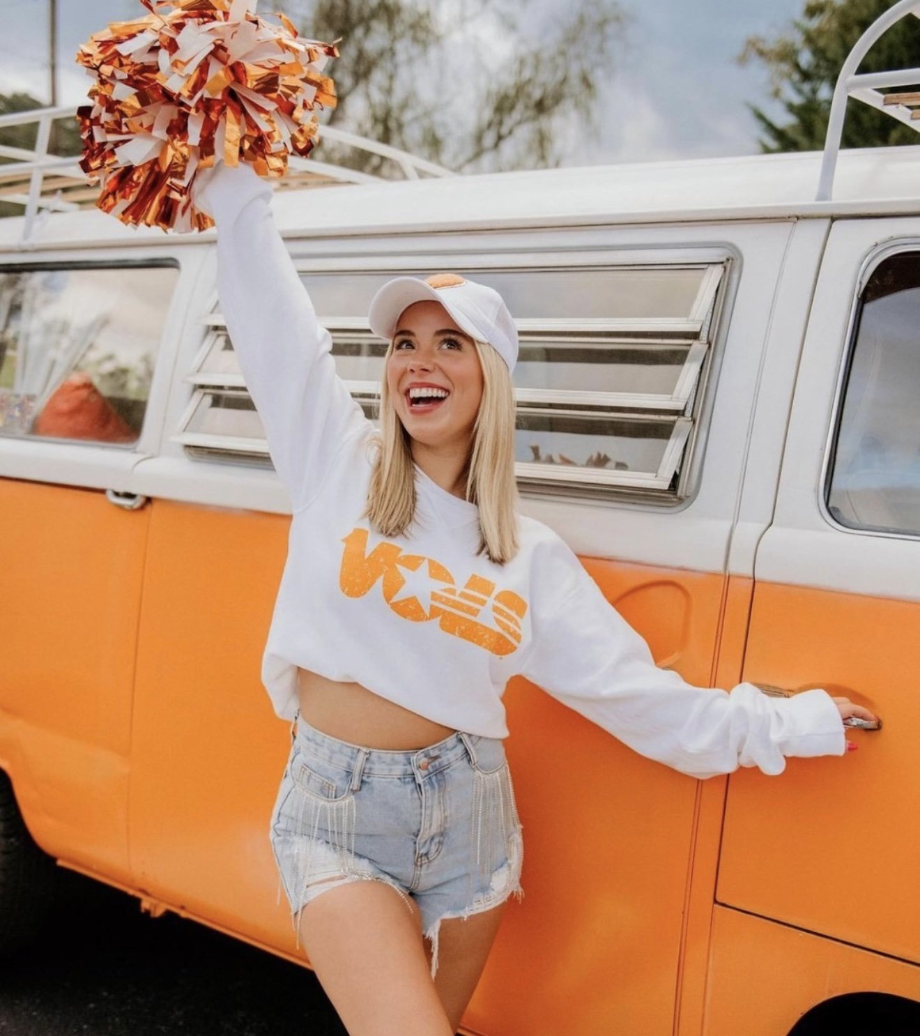 Woman in Tennessee Volunteers sweatshirt with pom-pom beside Nancy, orange VW bus, brand content shoot
