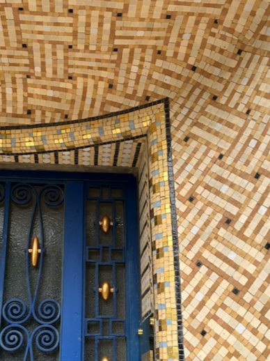 Close-up of a building corner with patterned brickwork, a blue metal gate, and a golden door handle.