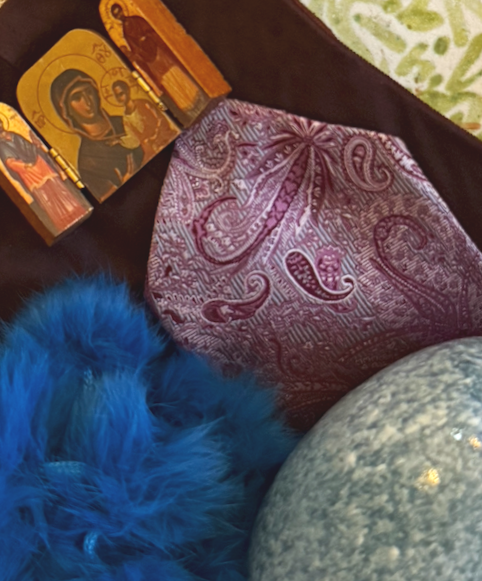 Religious icons, a purple patterned cloth, a blue feathered object, and a gray marble-like sphere.