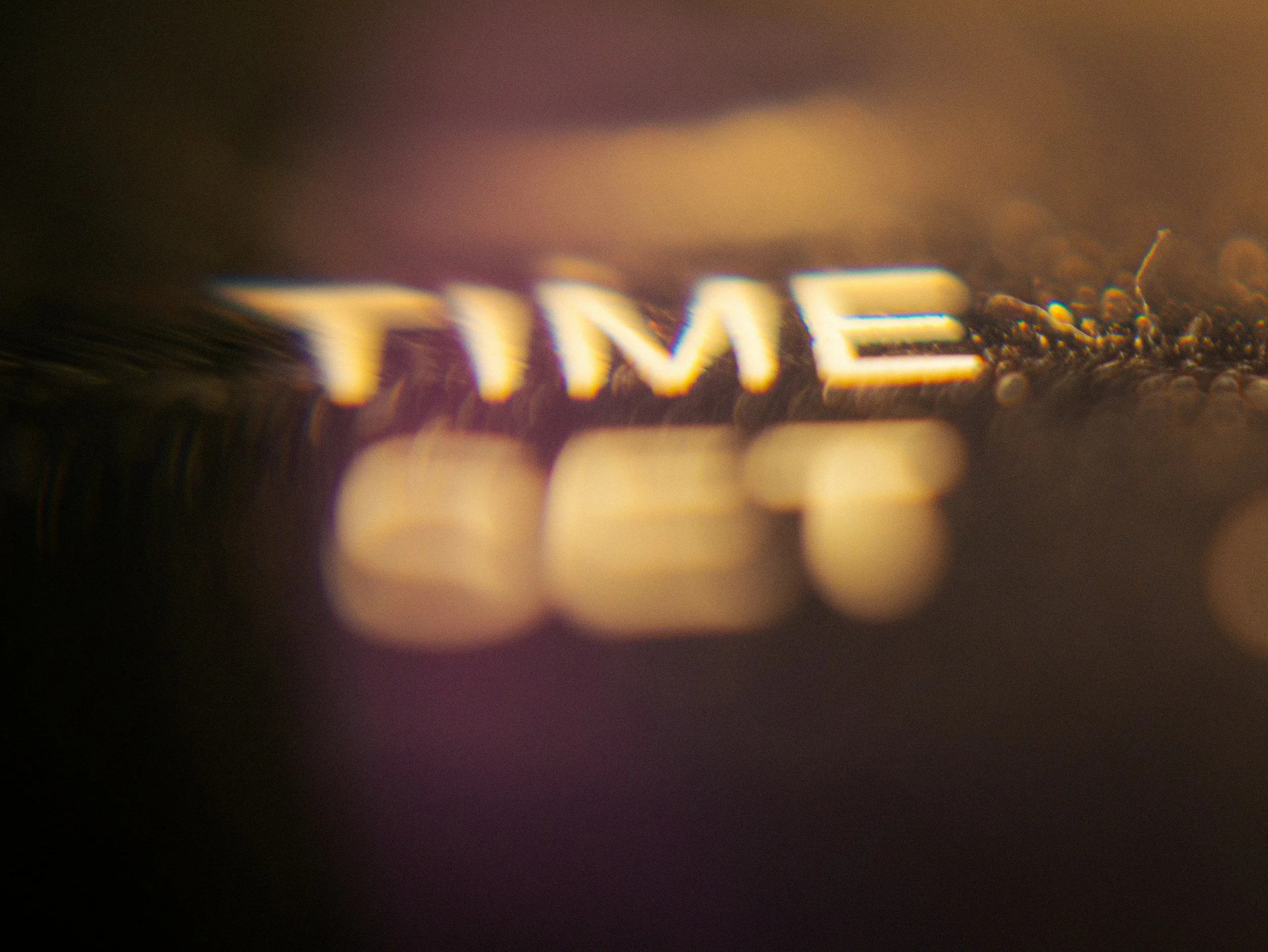 Close-up of the word 'TIME' illuminated on a metallic surface with blurred background.