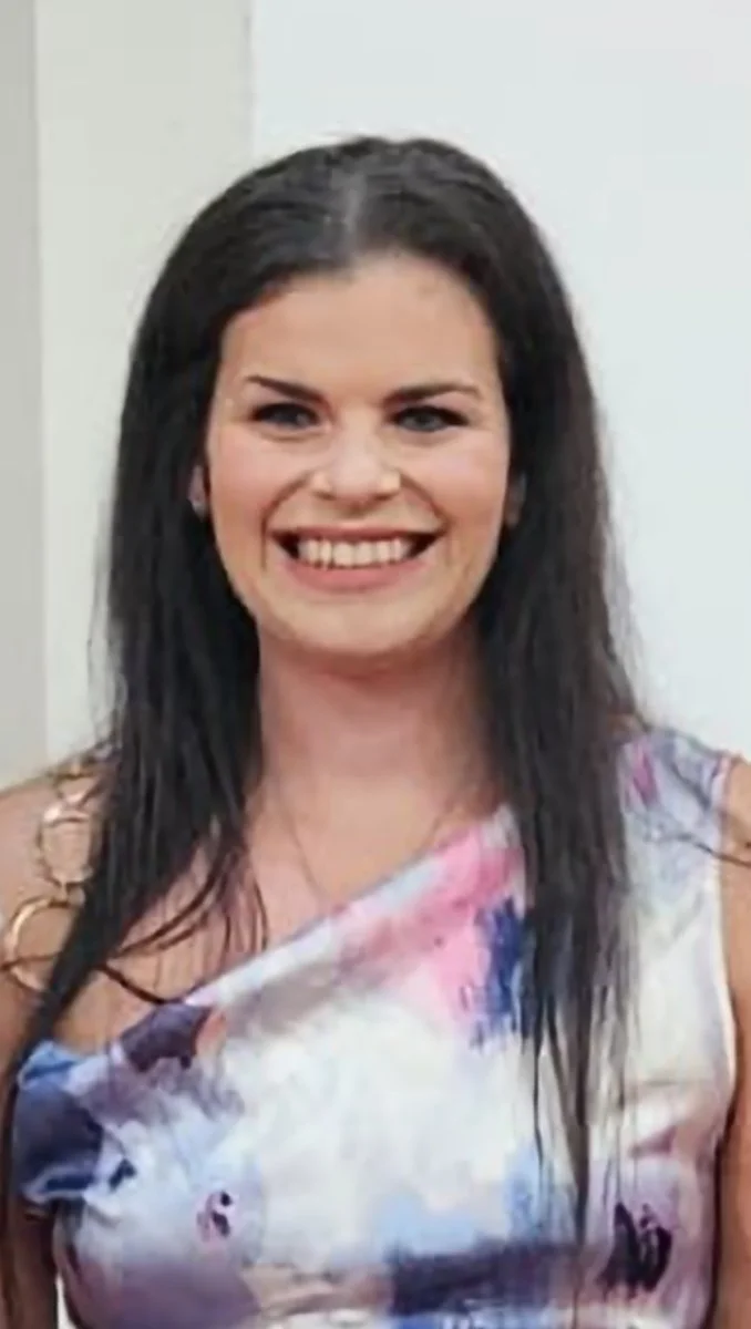 A woman with long dark hair smiling, wearing a colorful floral dress.