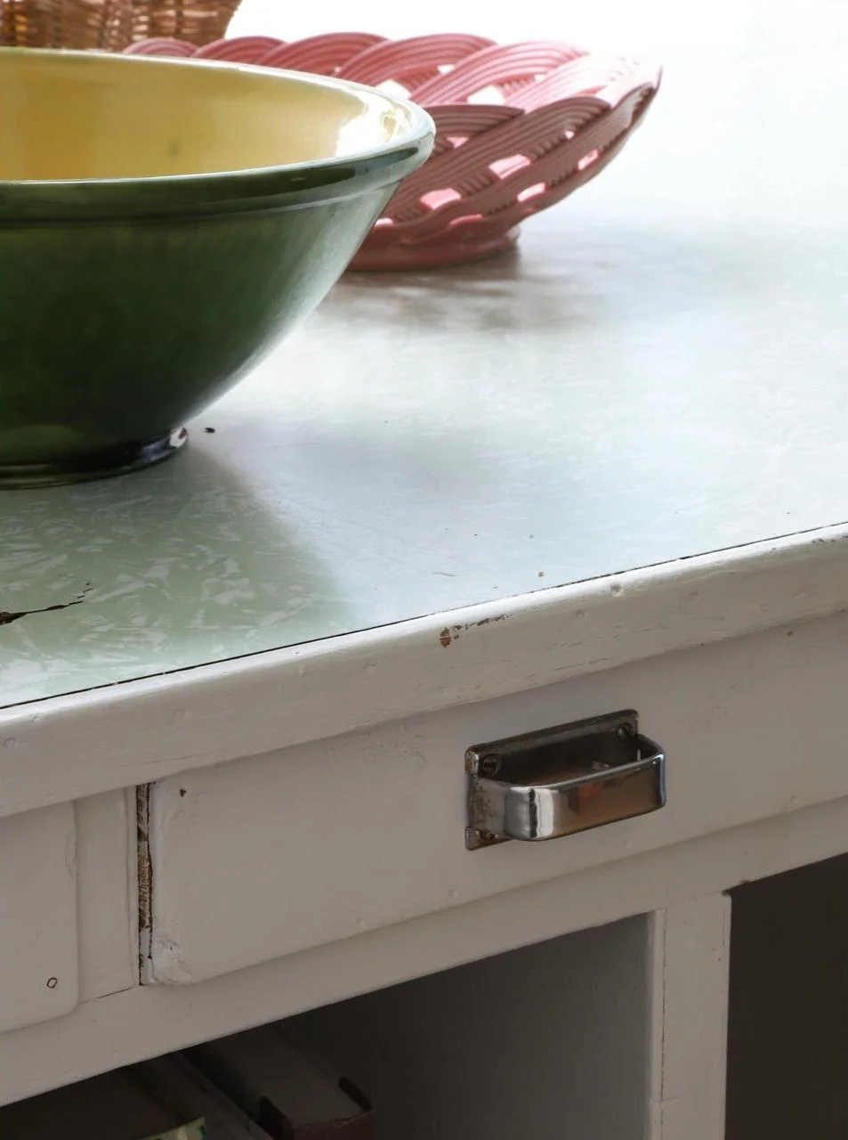 Bol vert posé sur une table blanche, avec un panier rose en arrière-plan et un tiroir à poignée métallique.