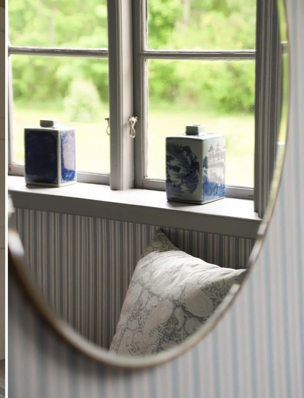 Deux boîtes décoratives en porcelaine bleue posées sur le rebord d’une fenêtre, dans une chambre lumineuse donnant sur un jardin verdoyant.
