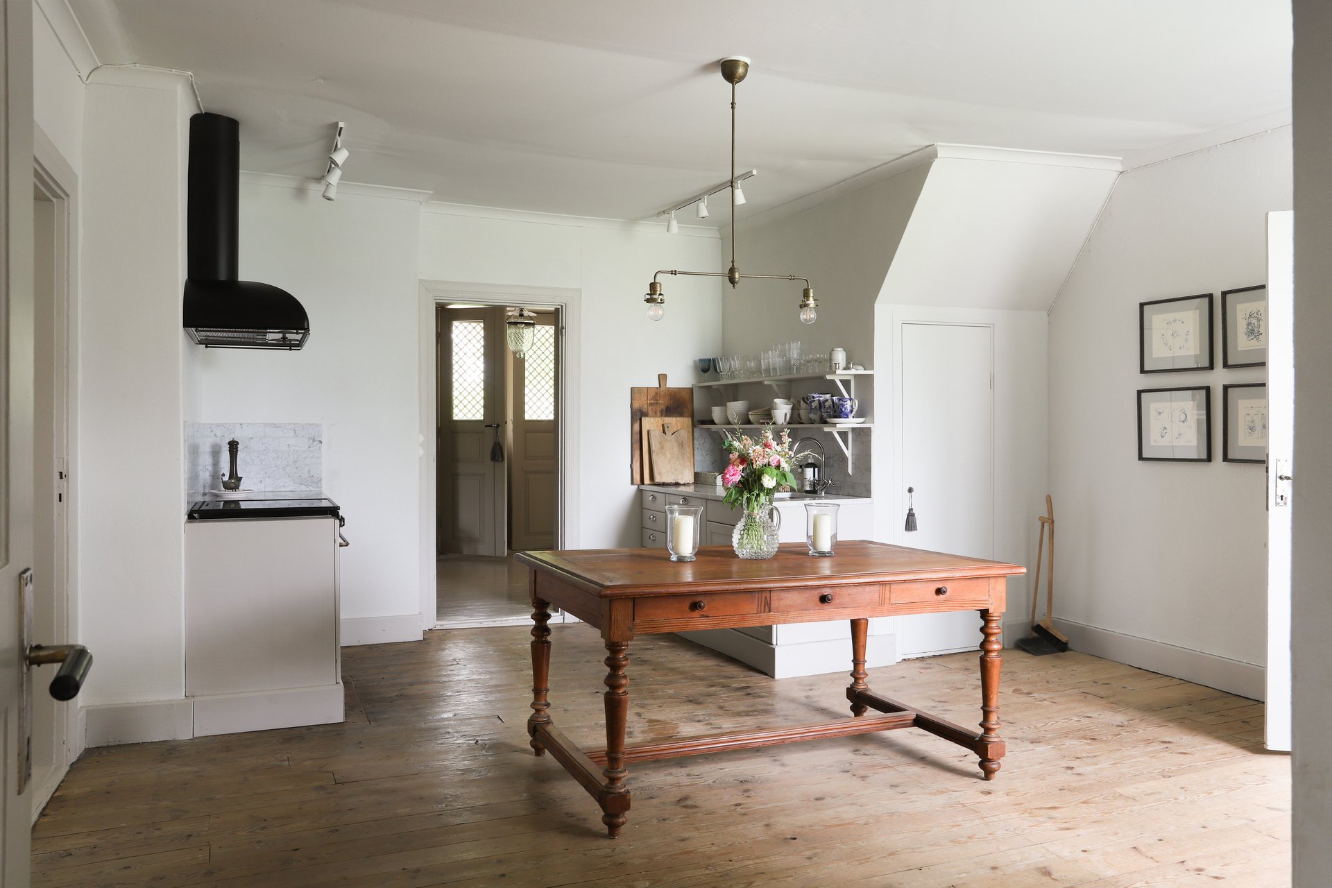 Cuisine lumineuse blanche avec îlot central en bois, cuisinière noire, vaisselle sur étagères et bouquet de fleurs.