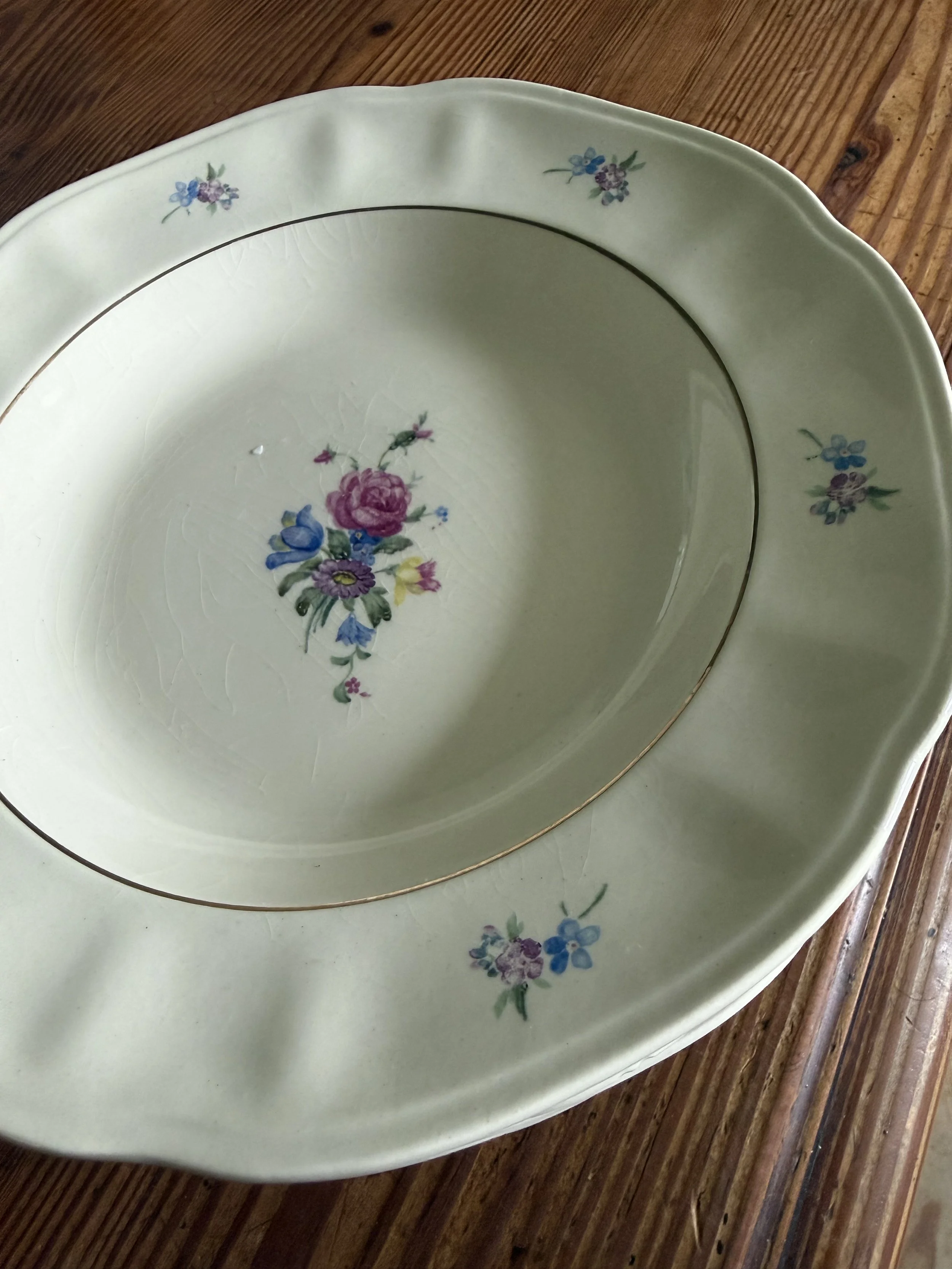 Grand plat de service en porcelaine blanche à bord doré, décoré de motifs floraux colorés, posé sur une table en bois.