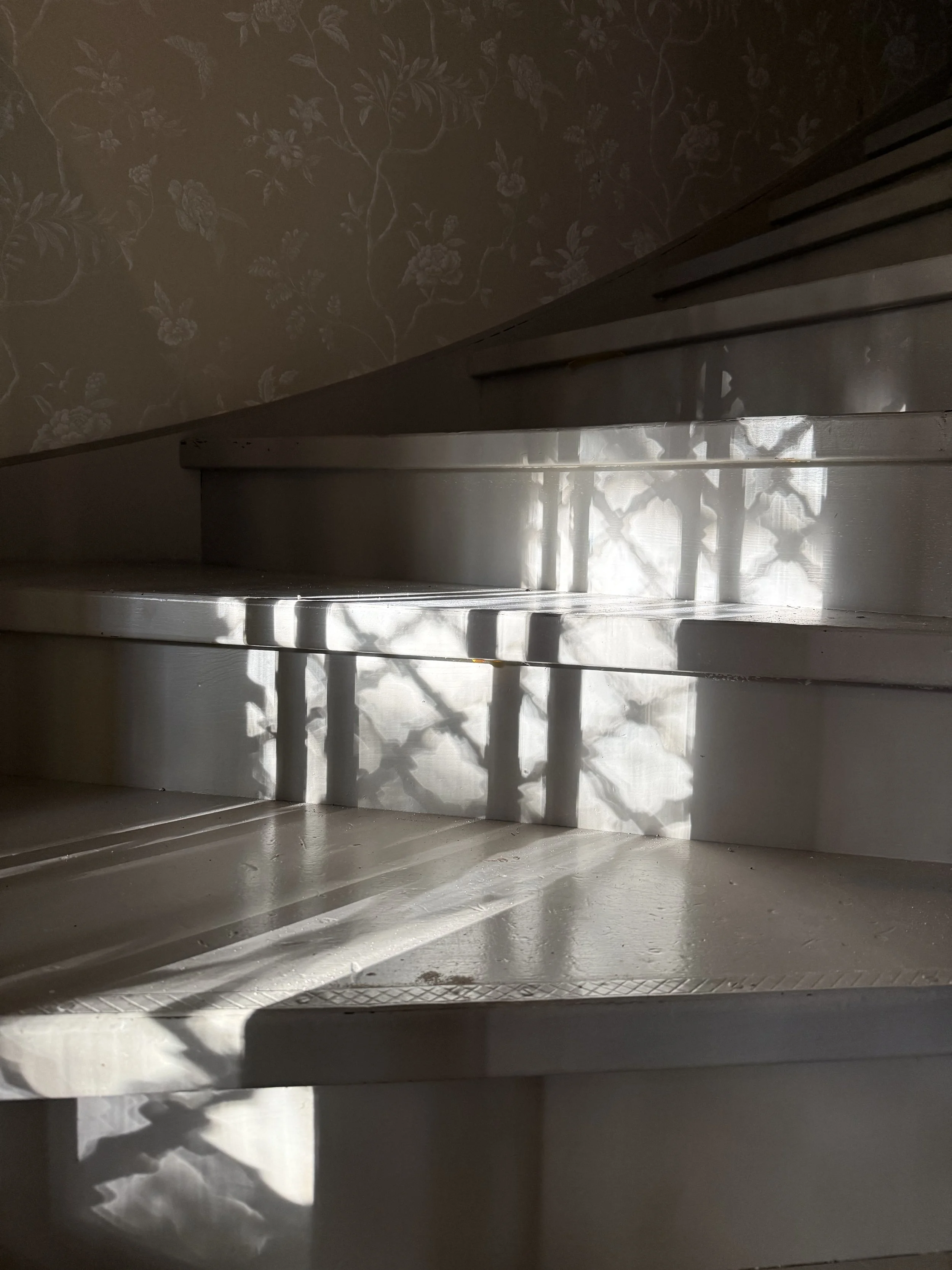 Intérieur d’un ancien four avec parois métalliques, papier peint floral et rayons de soleil projetant des ombres.