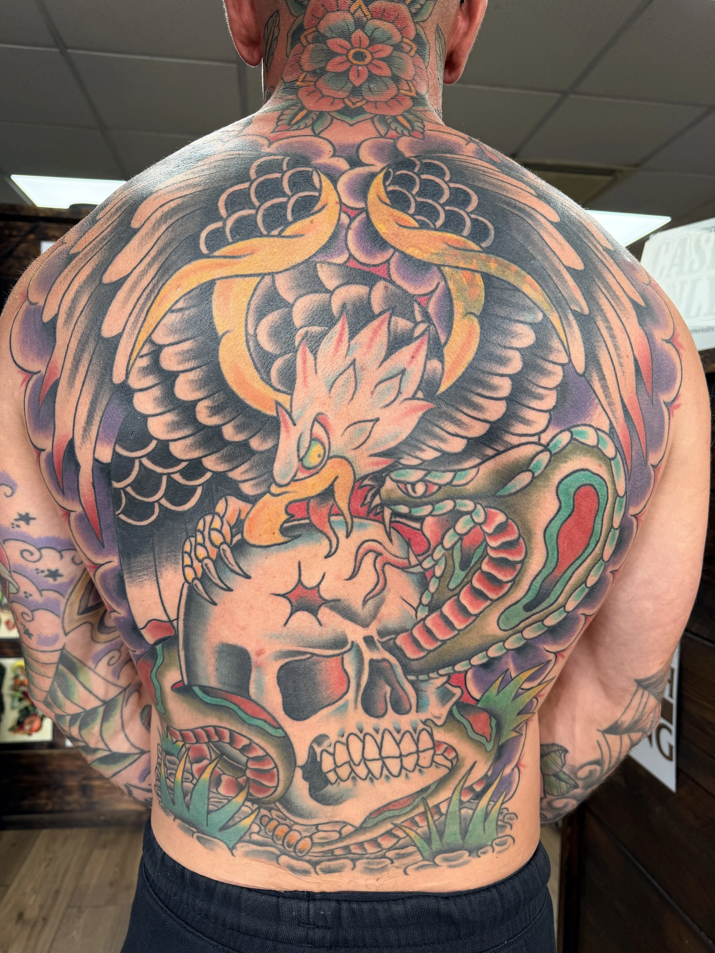 Colorful back tattoo of a dragon coiled and facing downward, with flames, clouds, and other traditional Japanese-style design elements.