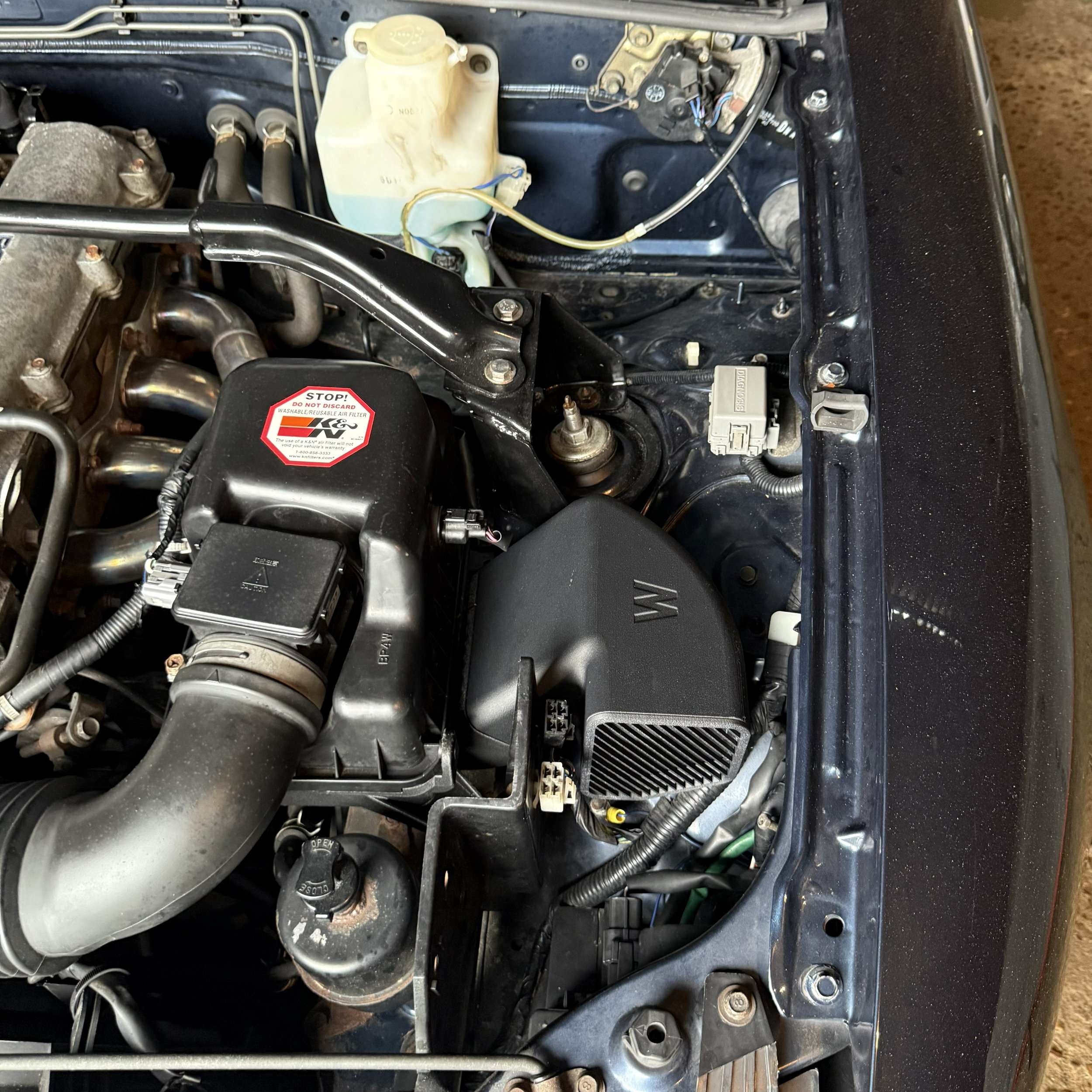 Vue de l'intérieur du compartiment moteur d'une voiture, montrant divers composants mécaniques et électriques.