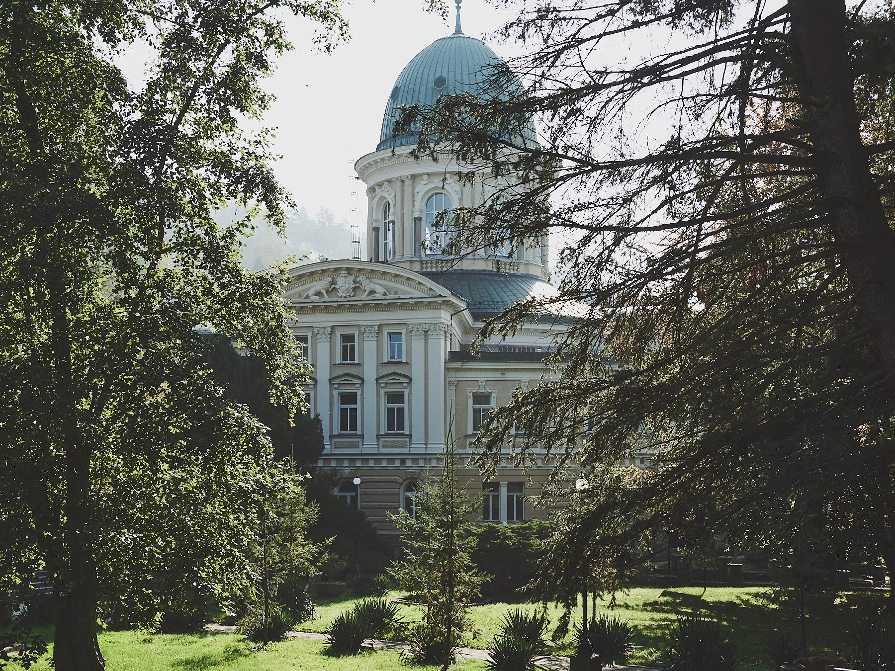 Ornate historic building with a large domed roof surrounded by trees and landscaped gardens