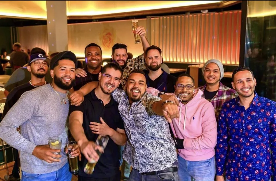 Group of 11 friends posing with drinks at a warmly lit restaurant or bar