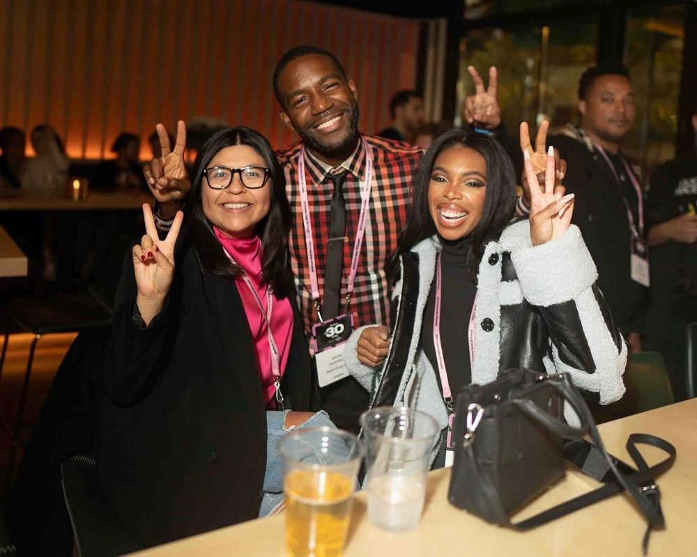 Three smiling event attendees pose together, flashing peace signs at a social gathering.
