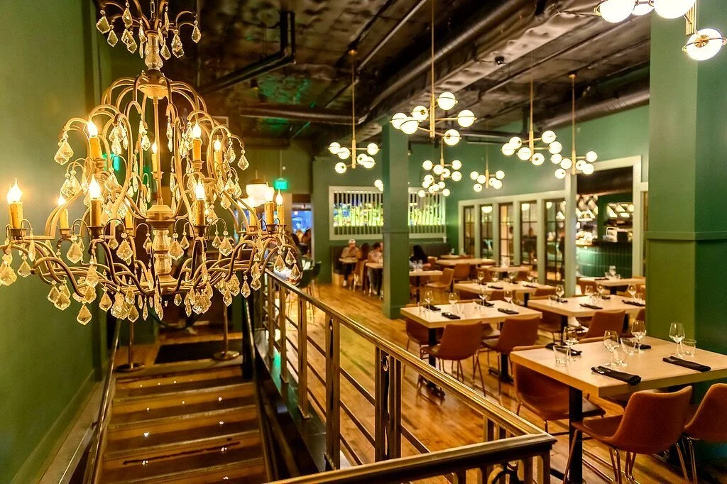 Elegant green restaurant interior with crystal chandeliers, modern globe pendant lights, and neatly set dining tables.