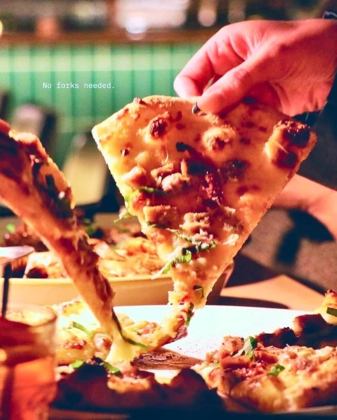 Hand lifting a slice of pepperoni pizza with melted cheese and herbs from a plate