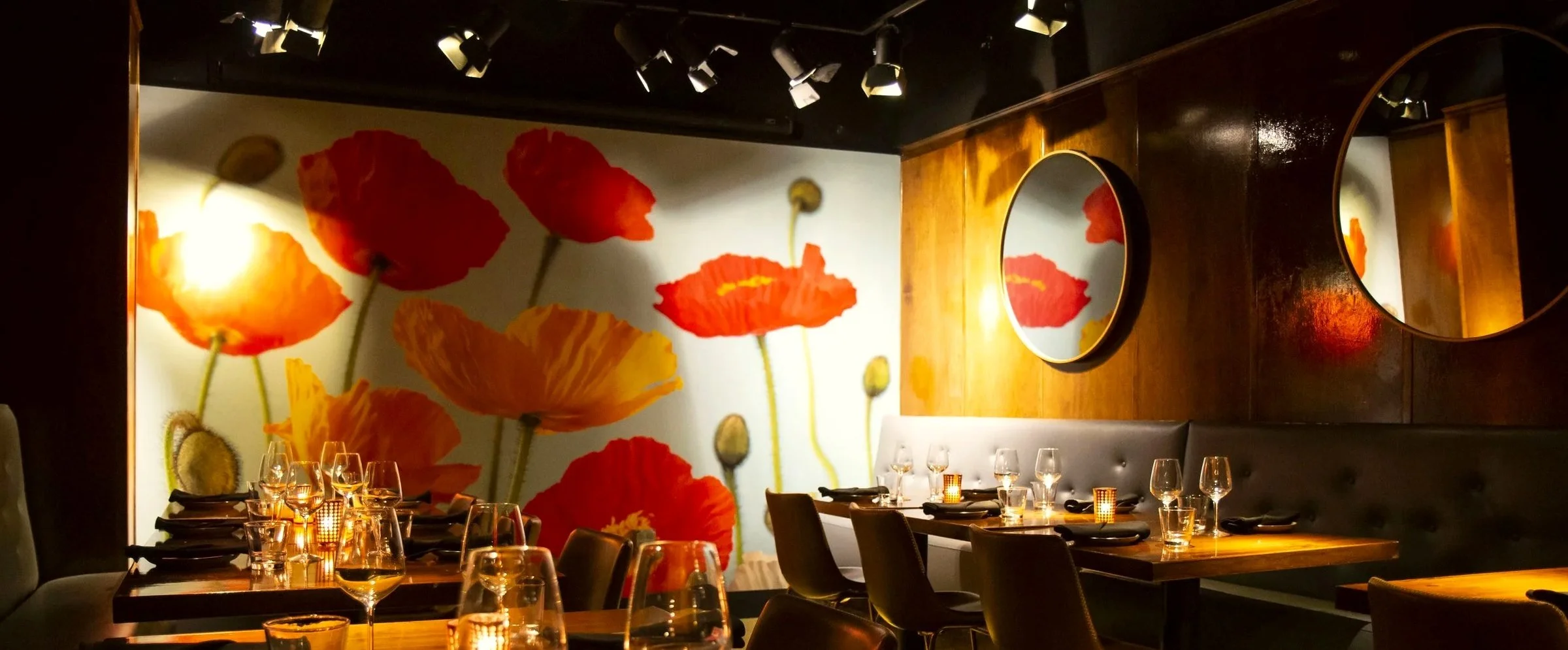 Upscale restaurant dining room with candlelit tables, wine glasses, poppy flower wall art, and round mirrors