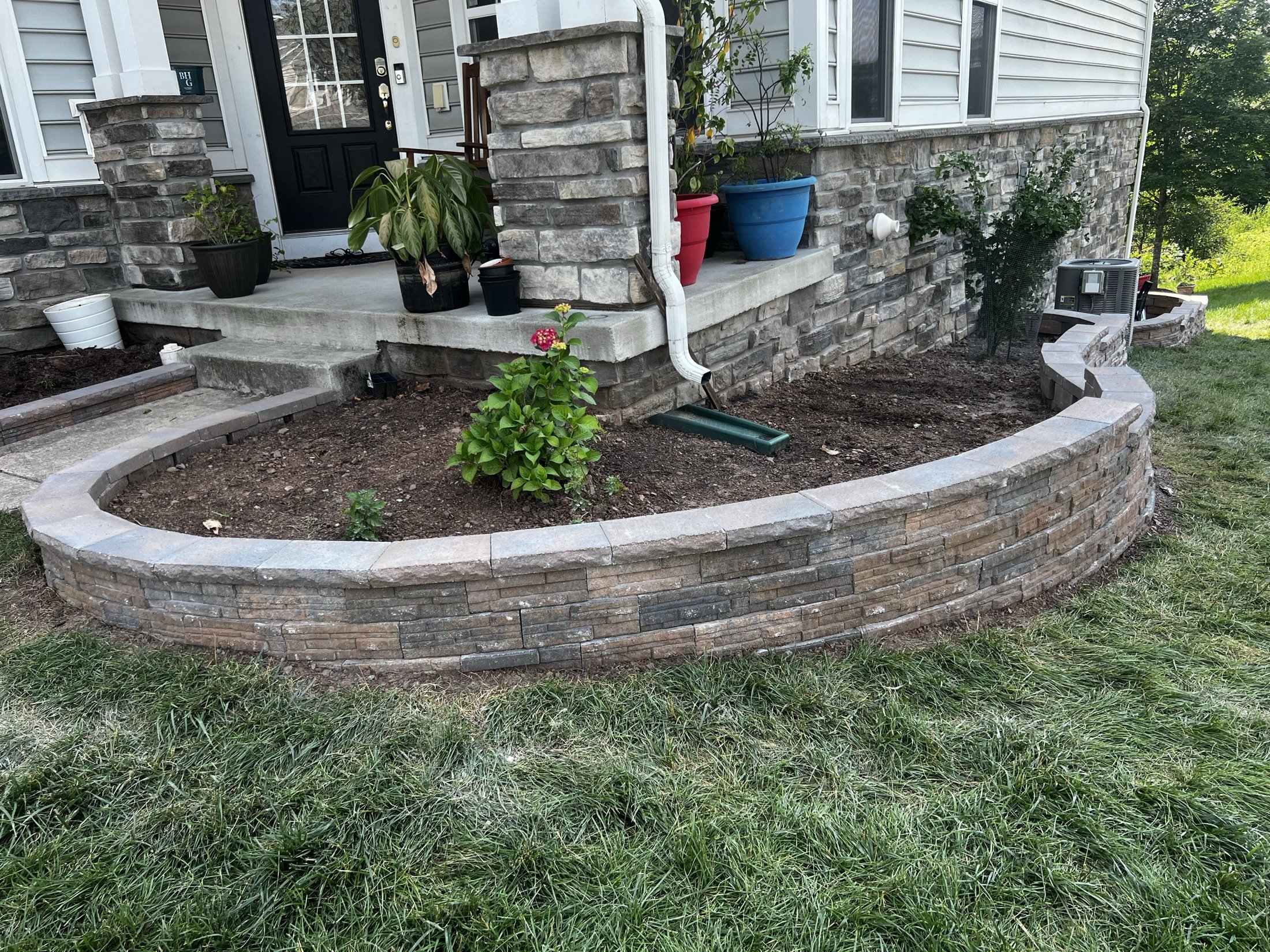 Raised stone garden bed with flowering plants beside a stone-clad home porch