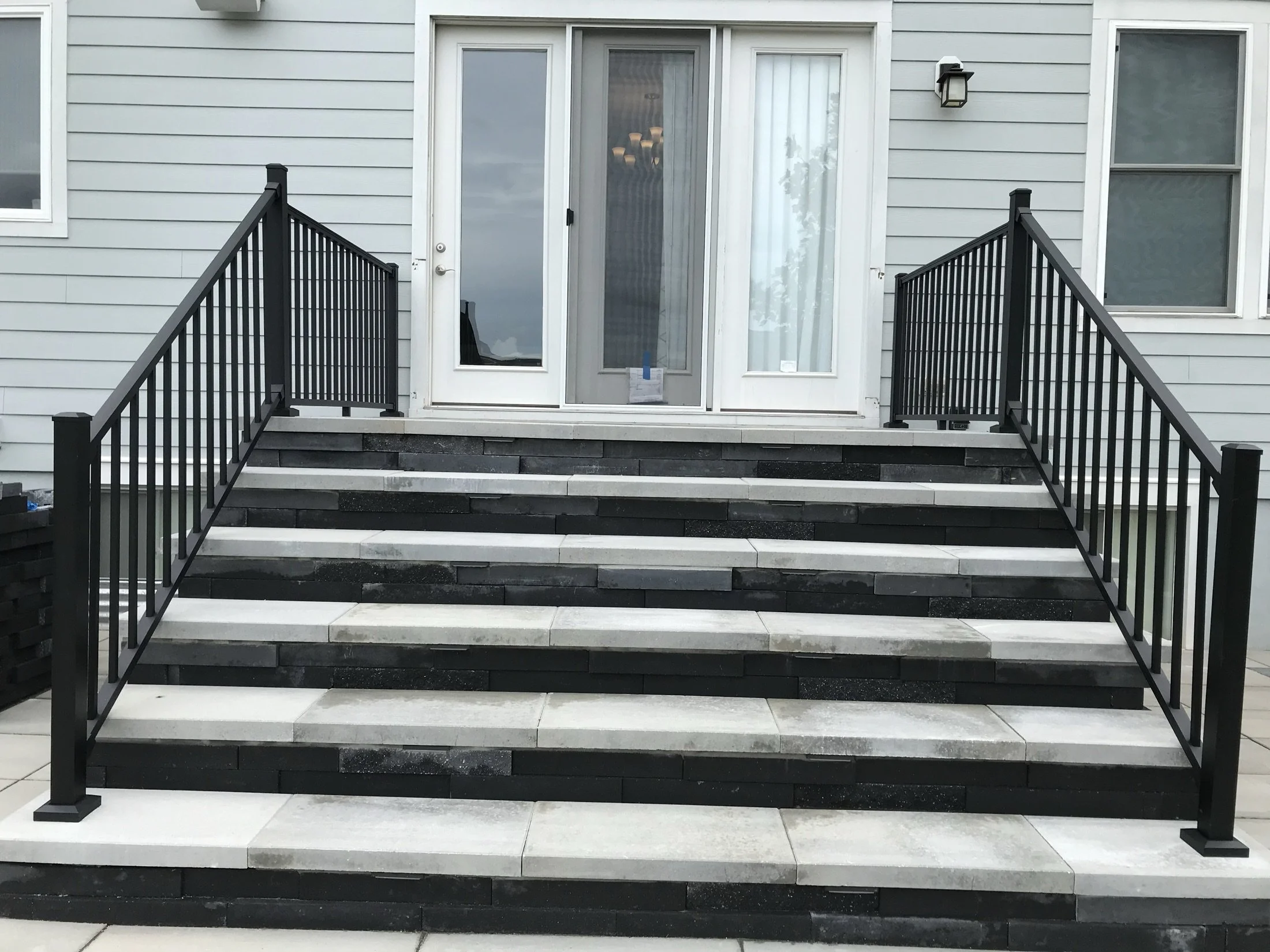 Modern black-and-white stone front steps with black metal railings leading to a glass-paneled entrance door.