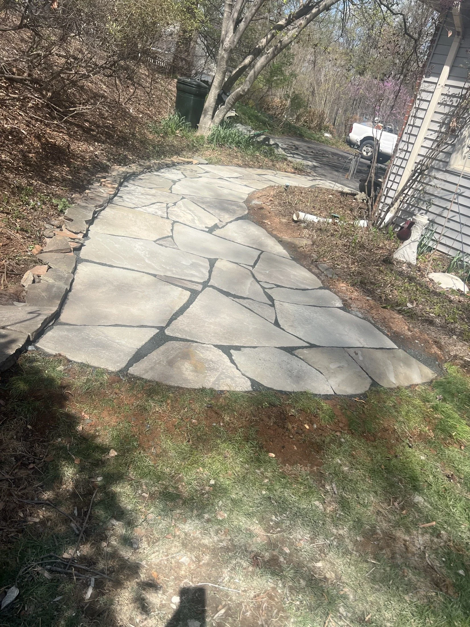 Flagstone walkway leading through a wooded residential yard beside a house and driveway