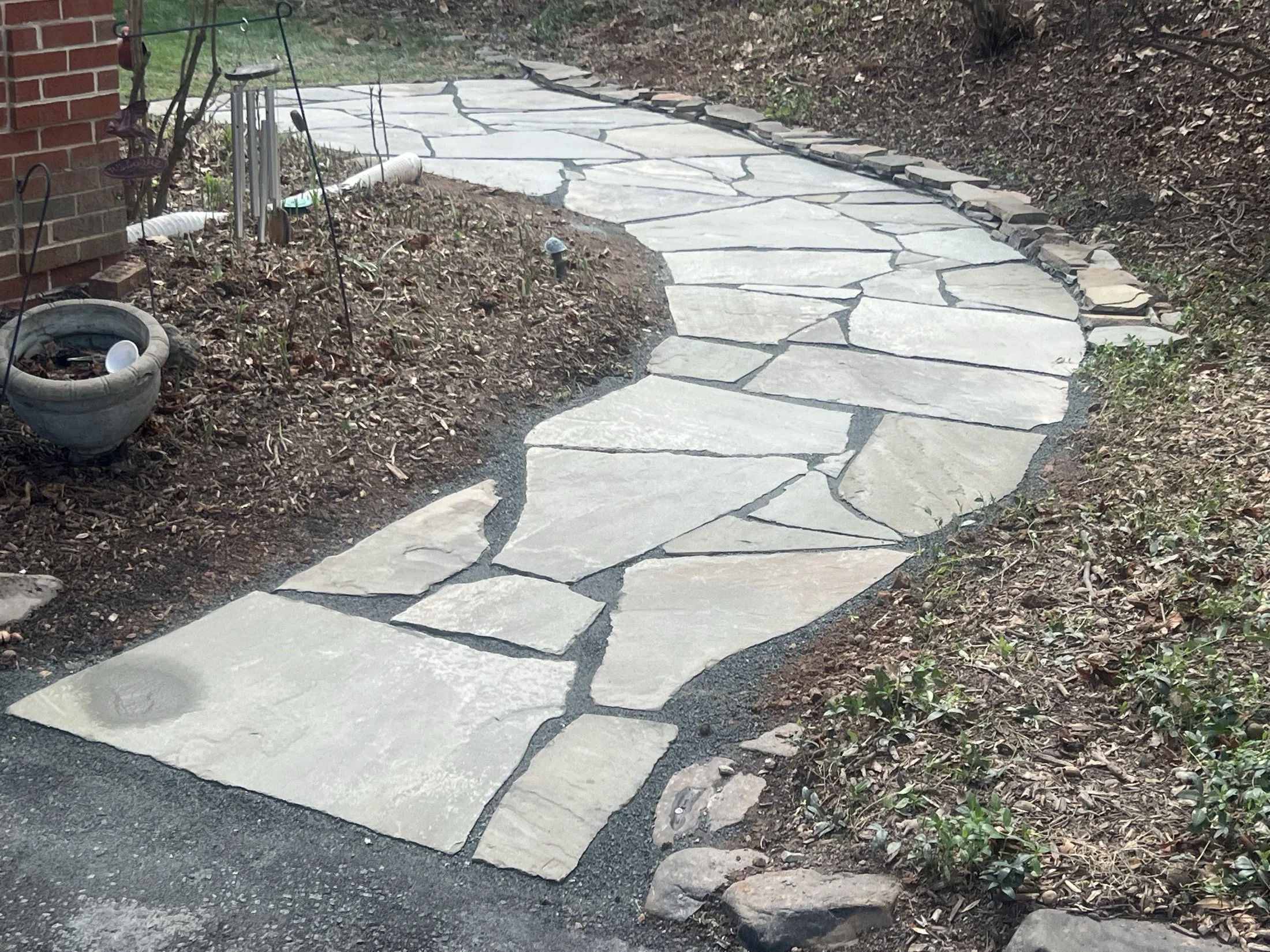 Irregular flagstone garden walkway bordered by rocks and mulch beside a brick house