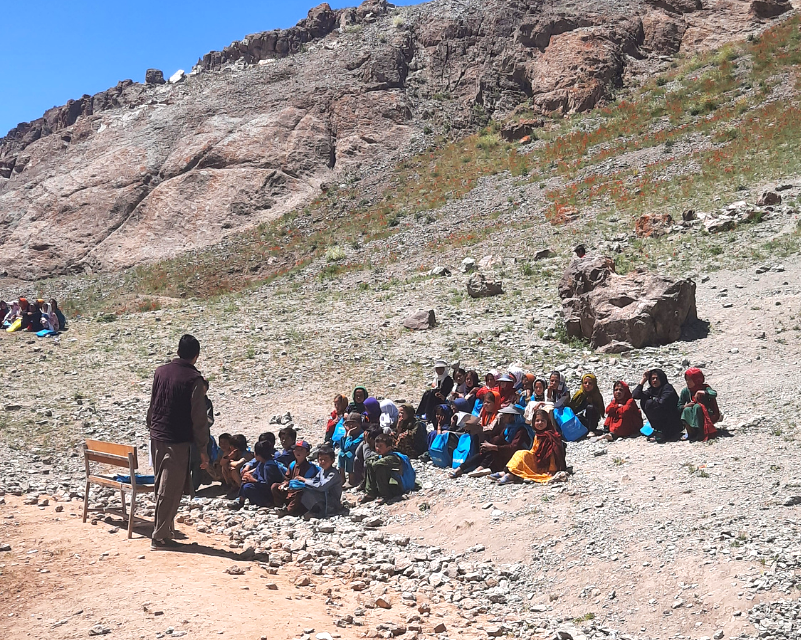 Schoolchildren gather for a lesson outdoors after flooding damaged their school building. With the classroom temporarily displaced into the open air, teaching continues despite the disruption — a testament to the determination of children and educato