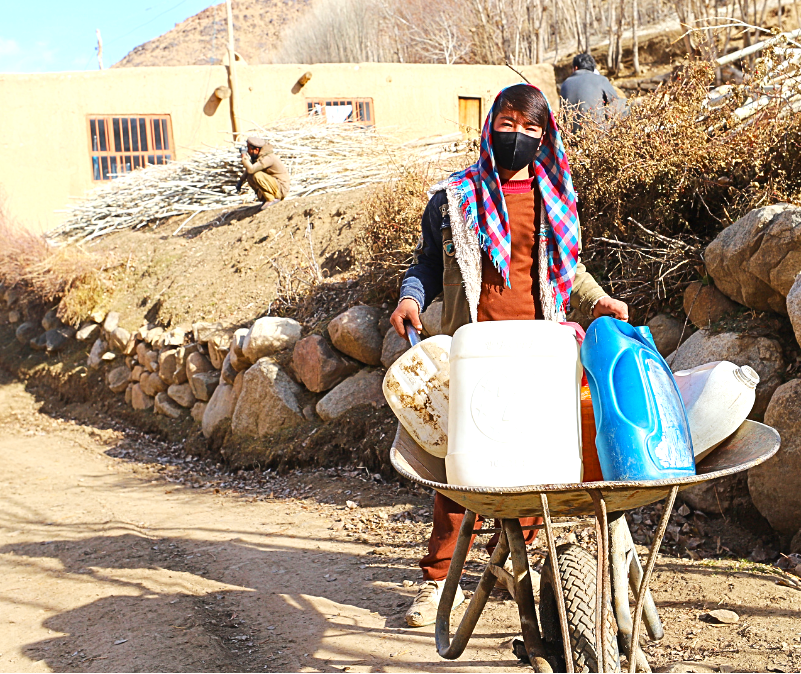 A boy transports water in a container balanced on a wheelbarrow through his village in Ghor. This everyday task reflects the practical challenges of accessing essential resources in rural communities, where water remains central to household life and