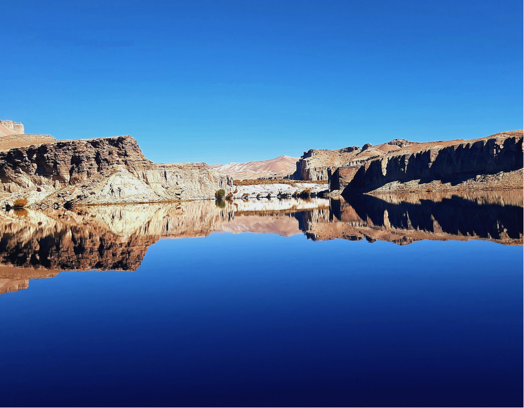 The deep blue waters of Band-e Amir stretch towards the horizon, reflecting the surrounding cliffs in an almost perfect mirror. Under the clear Afghan sky, the lake’s vivid colours and stillness create a striking landscape of scale, light and tranqui
