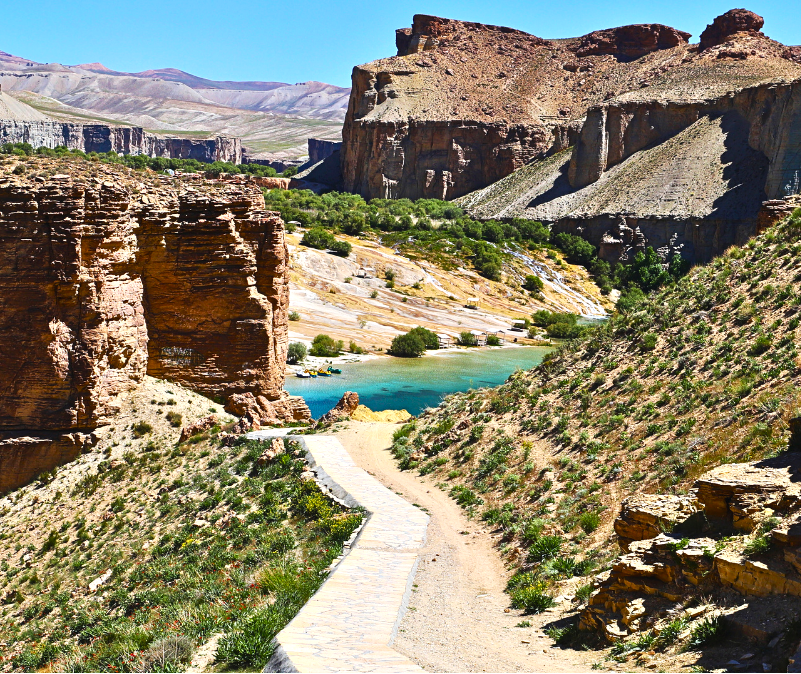 Seen from a footpath within Band-e Amir National Park, the lake appears in the distance, framed by rugged rock formations and the natural contours of the landscape. The path offers a closer encounter with this remarkable environment, where water, sto