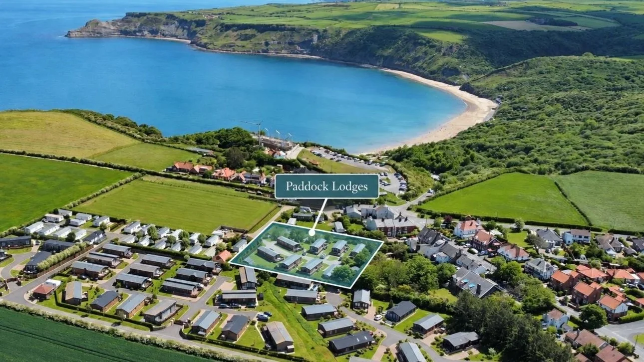 Aerial view of a coastal village, sandy bay, green farmland, and the highlighted Paddock Lodges development.