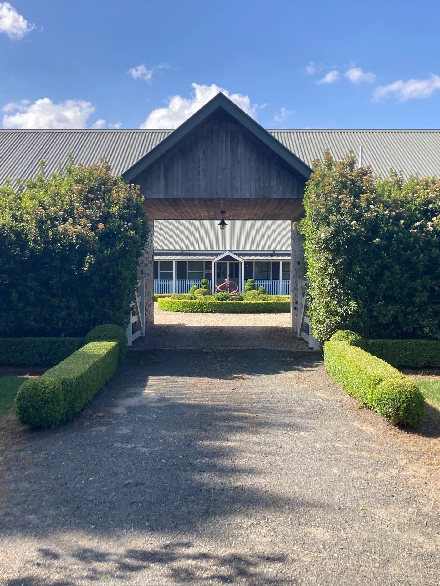 Formal garden entrance in High Range, NSW, framed by tall trimmed hedges and low box hedging, with sculpted topiary surrounding a country-style building.