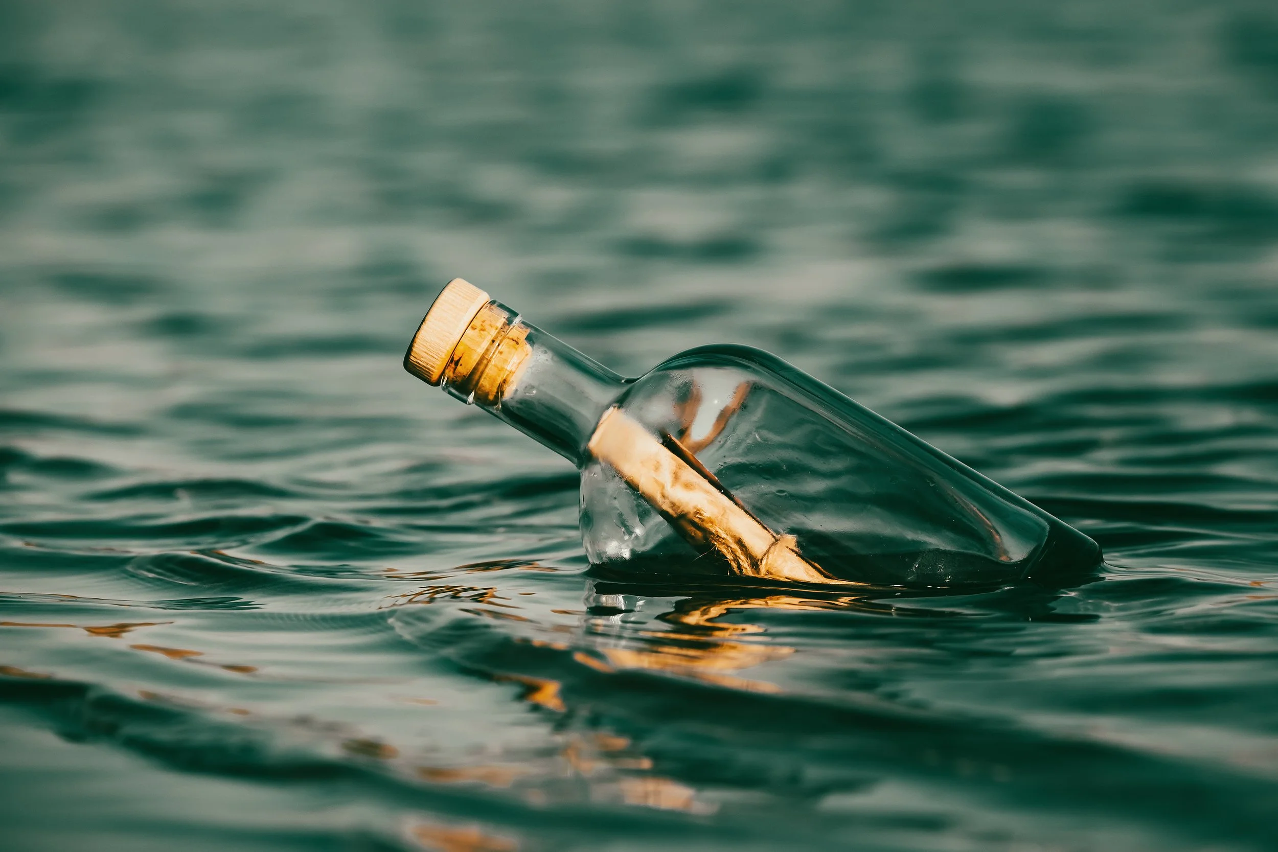 A glass bottle with a cork stuck in it floating on water, with a rolled piece of paper inside the bottle.