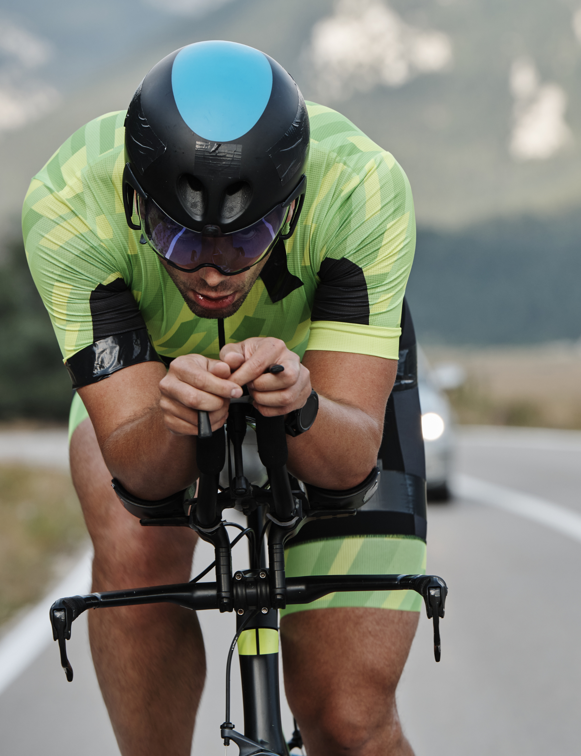 Cyclist in a neon green jersey and black helmet riding a road bike outdoors.