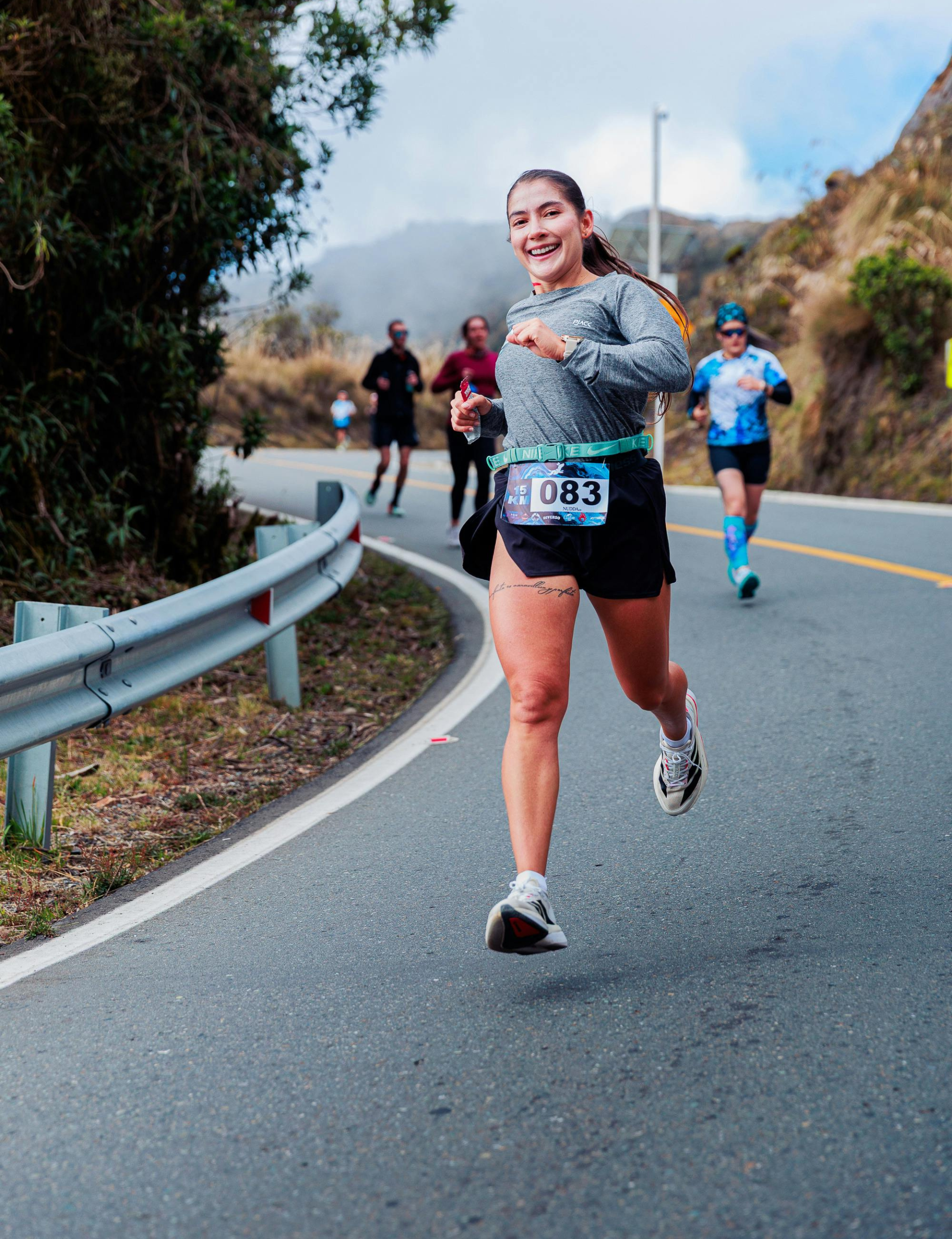 Smiling woman running in a road race with other runners on a scenic mountain road
