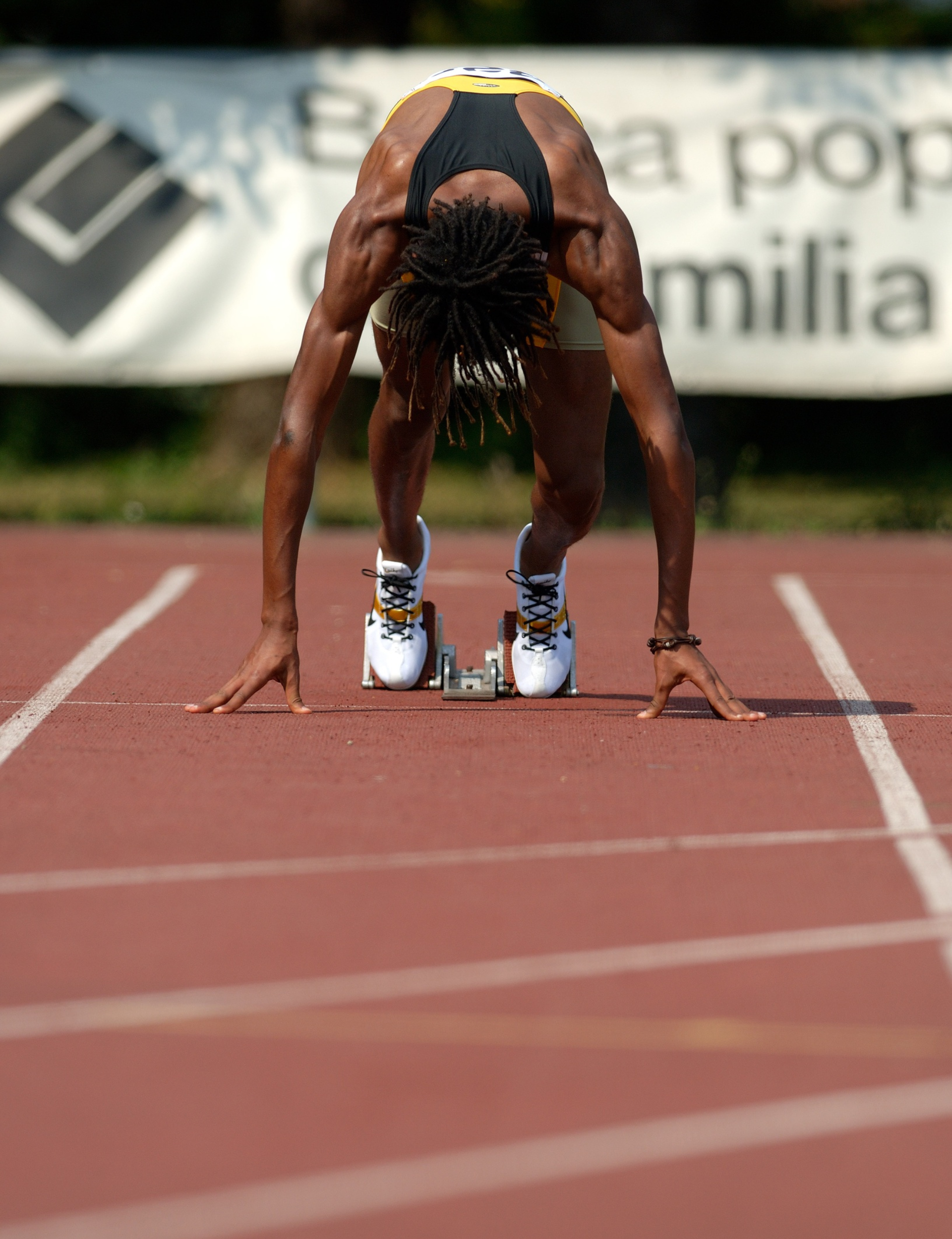 Sprinter with dreadlocks in starting position on a track, wearing spikes at the starting blocks.