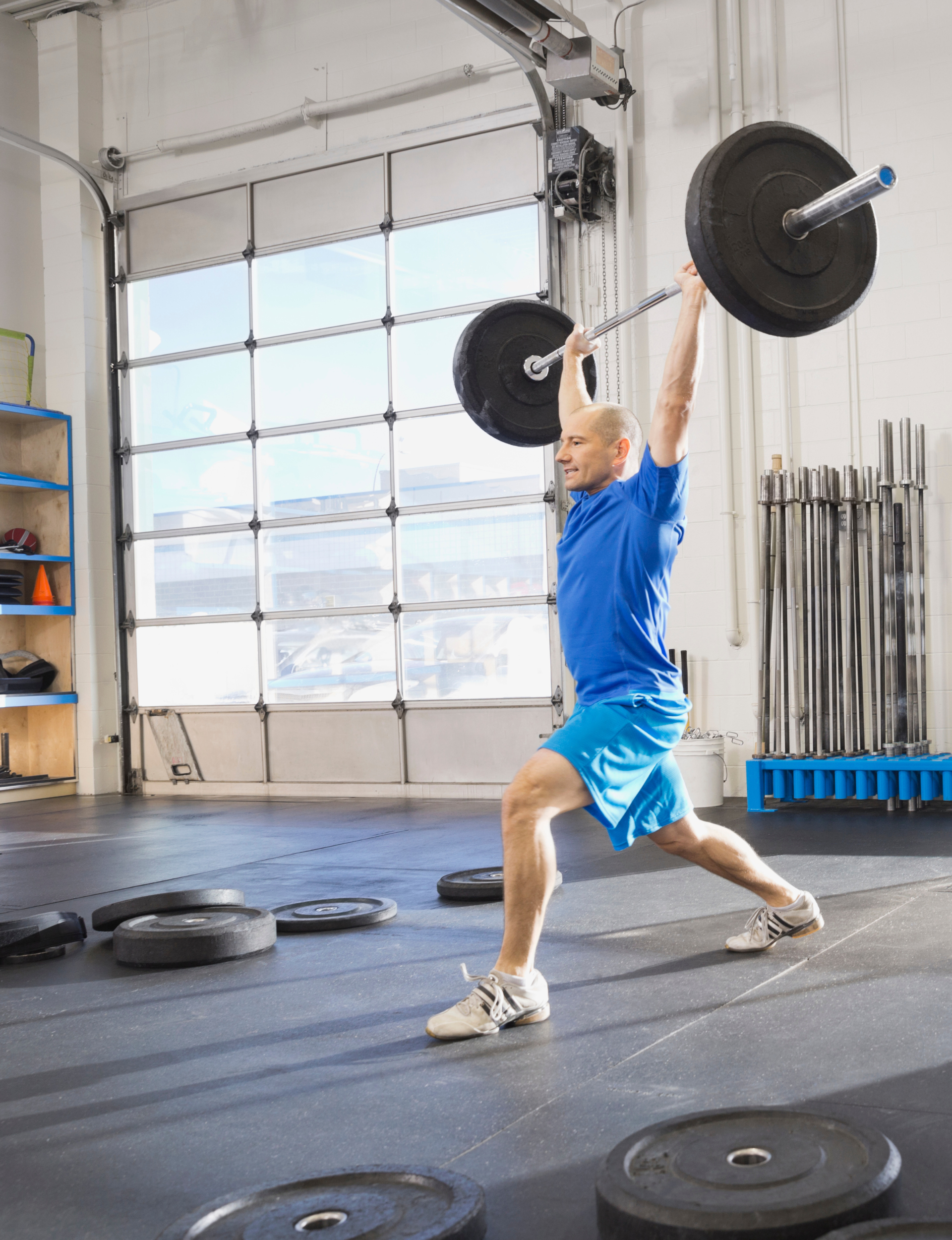 Man performing a barbell overhead lunge in a CrossFit gym