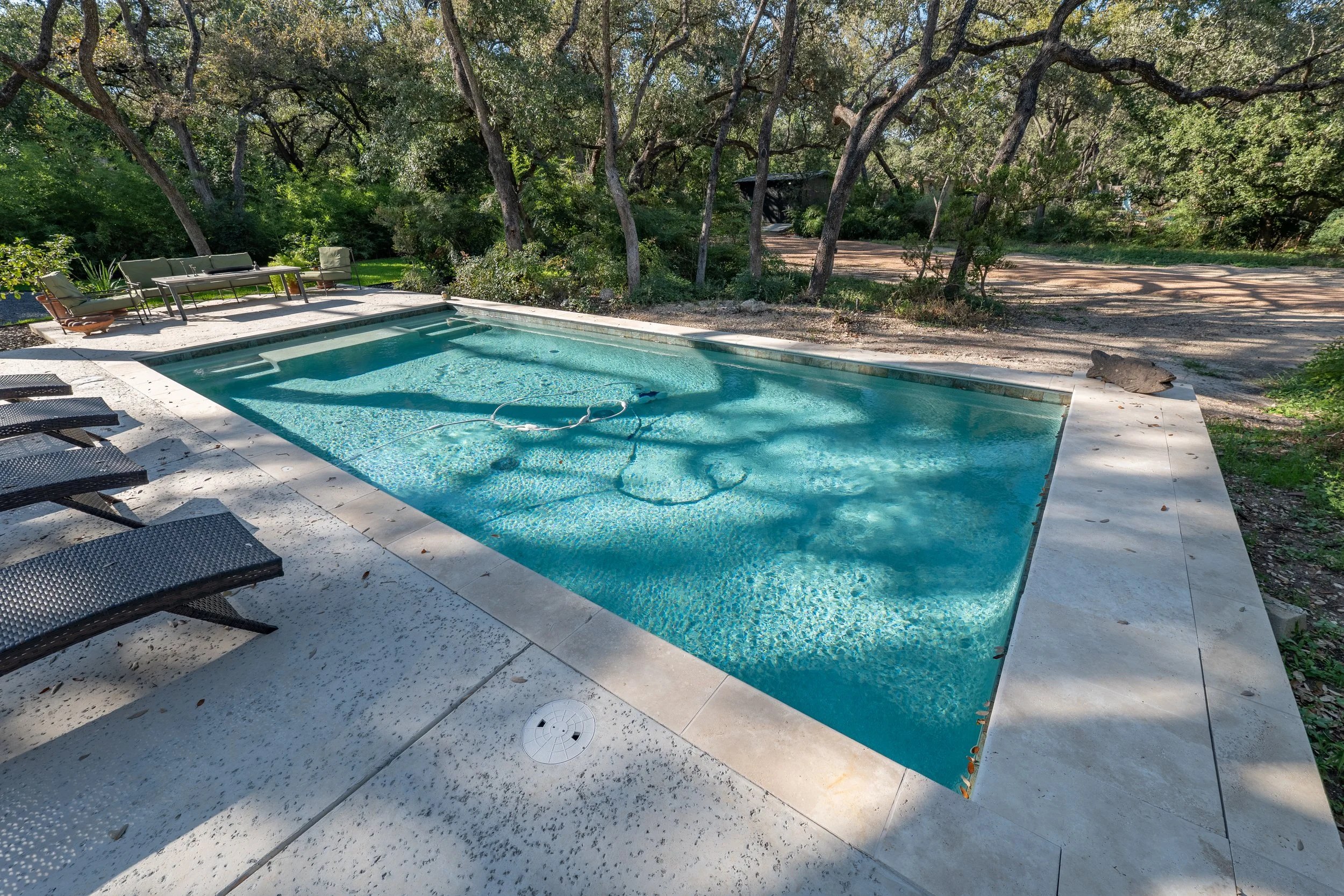 Outdoor swimming pool with lounge chairs and patio seating in a wooded backyard