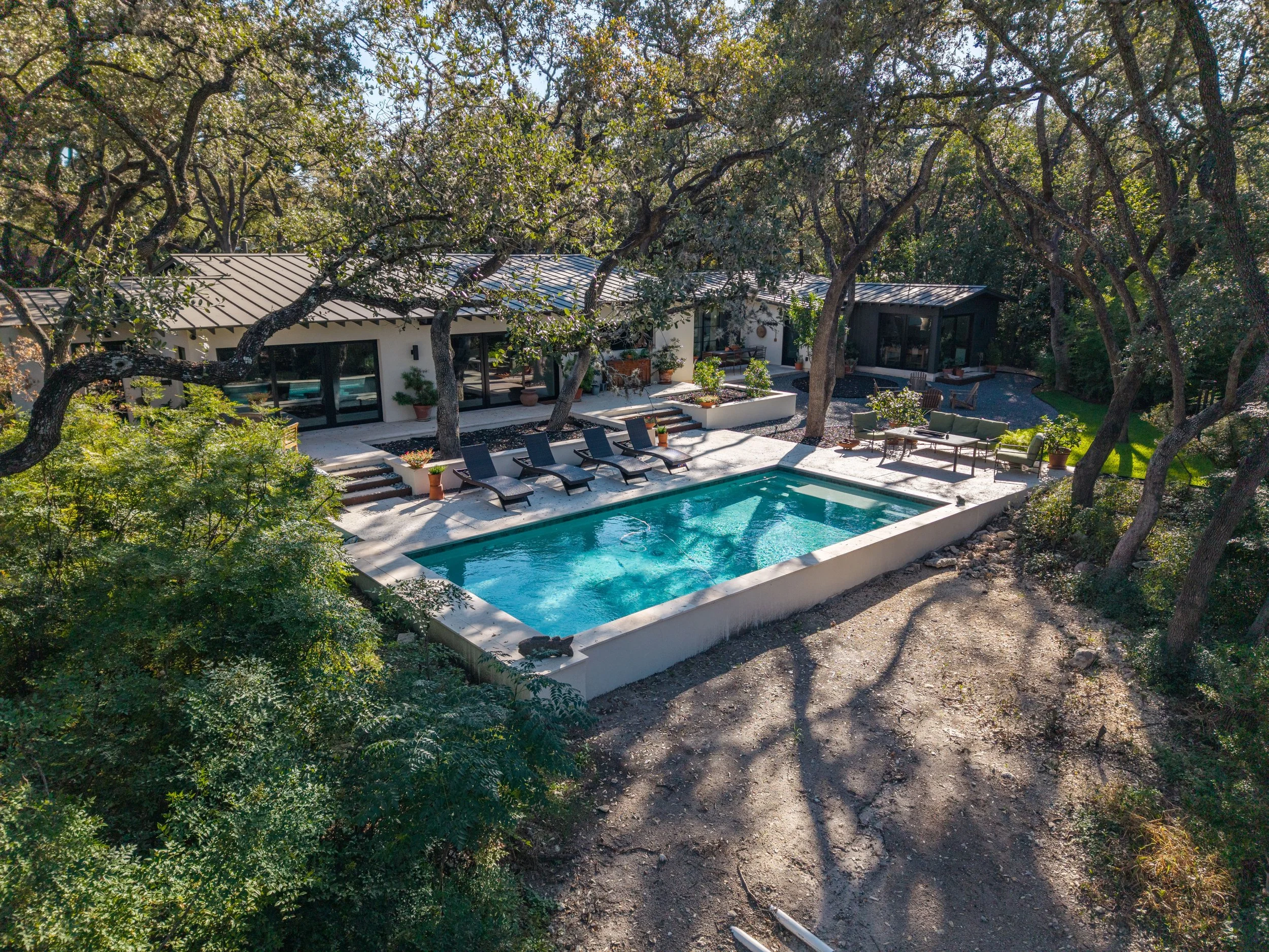 Modern home with a rectangular swimming pool, lounge chairs, and outdoor seating surrounded by mature trees