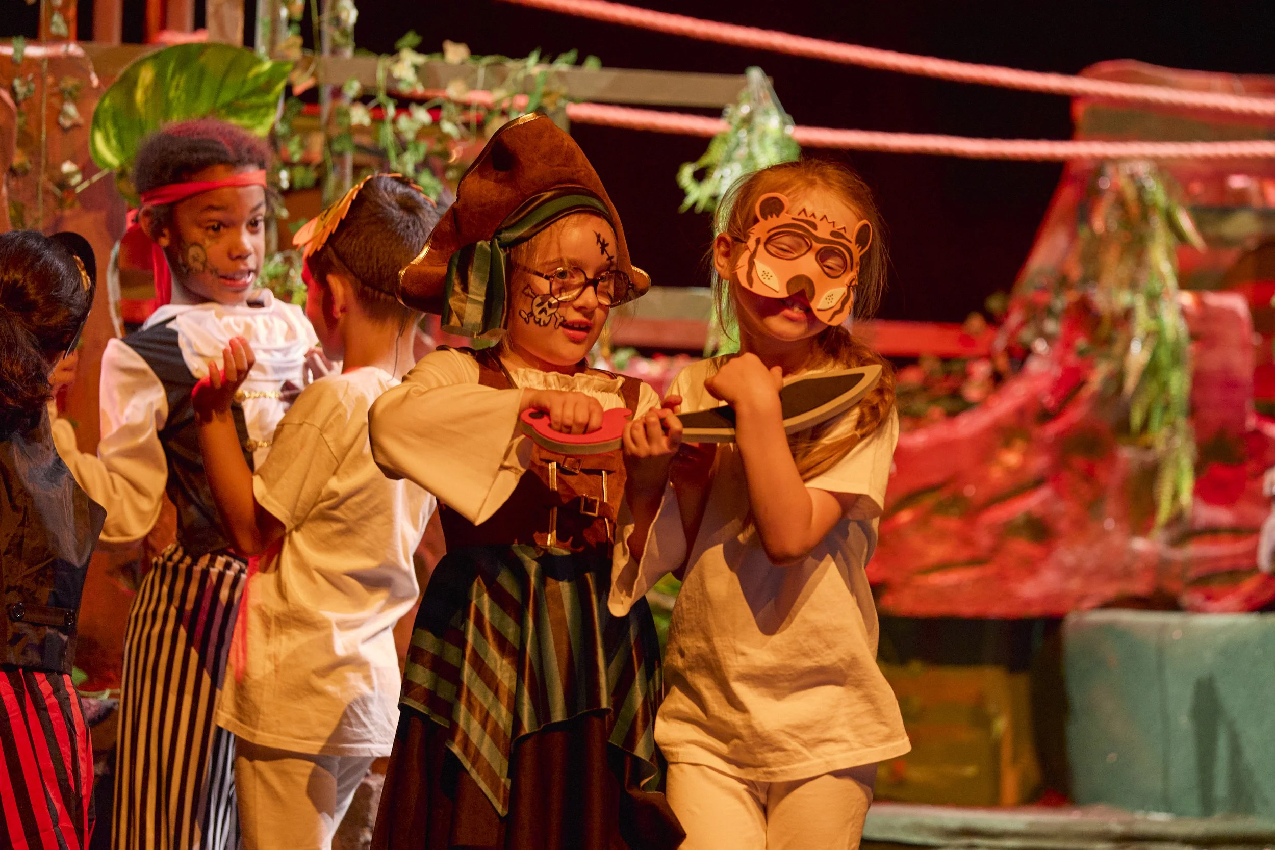 Enfants costumés, maquillés et armés d’épées jouant sur une scène décorée.