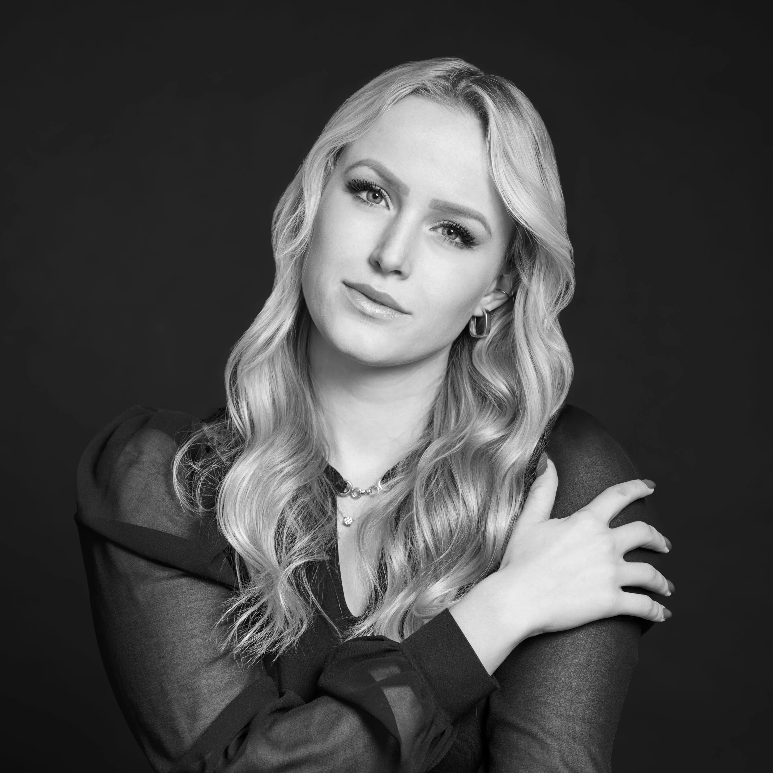 Portrait d'une femme blonde avec des yeux clairs, portant une veste sombre, confiance et élégance.