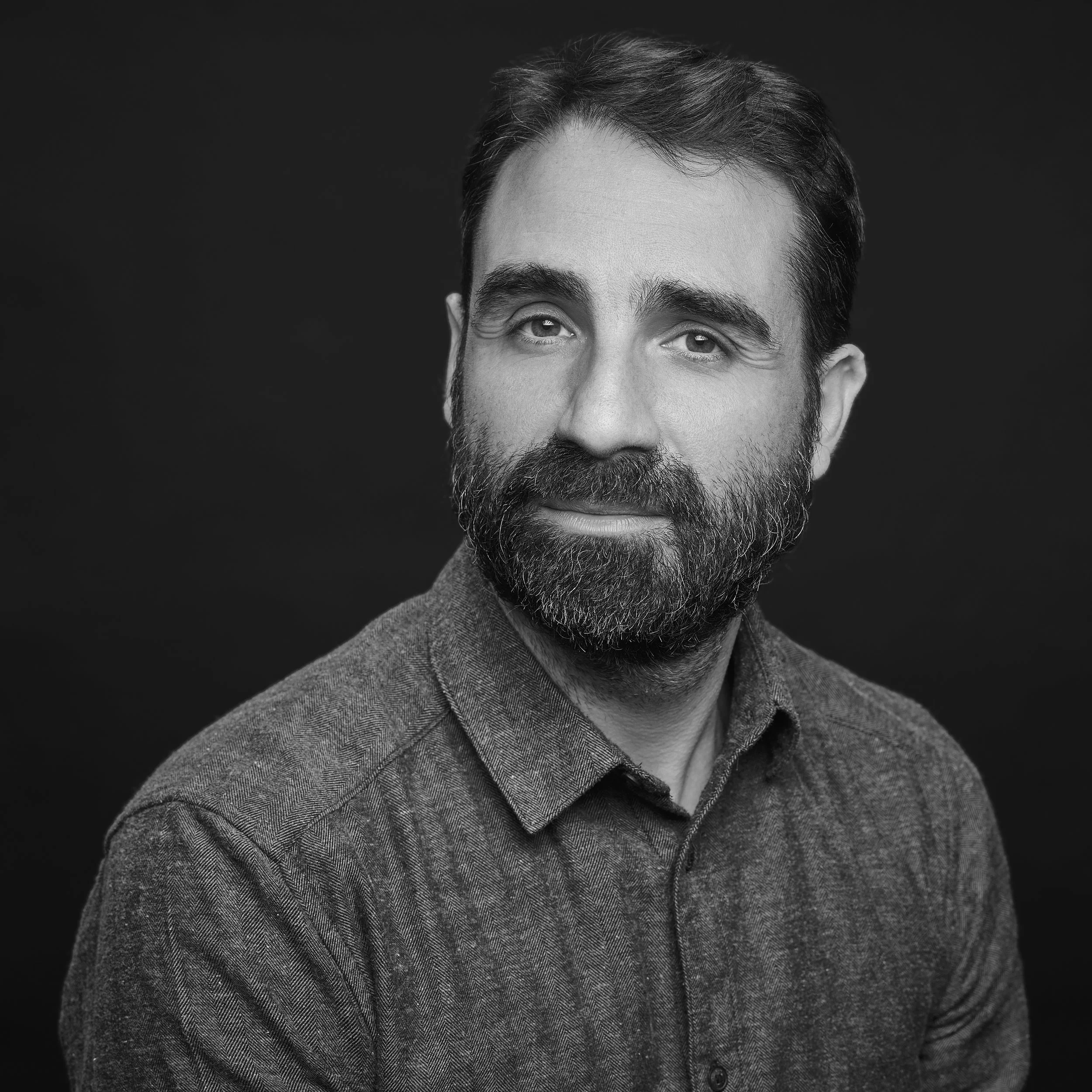 Portrait en noir et blanc d'un homme avec barbe, portant une veste en tweed.