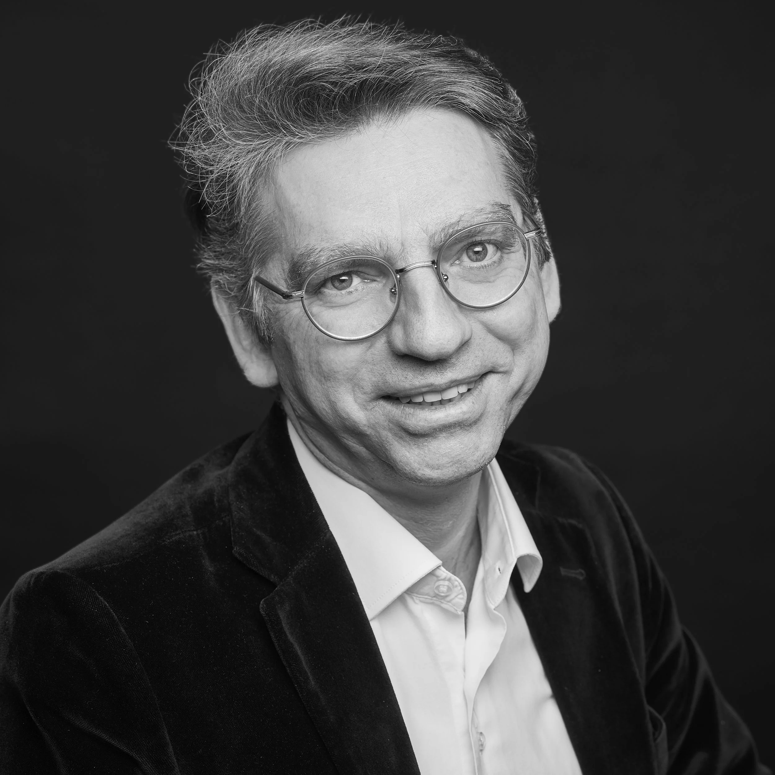 Photo en noir et blanc d'une personne âgée portant des lunettes rondes, avec des cheveux gris et une expression souriante.