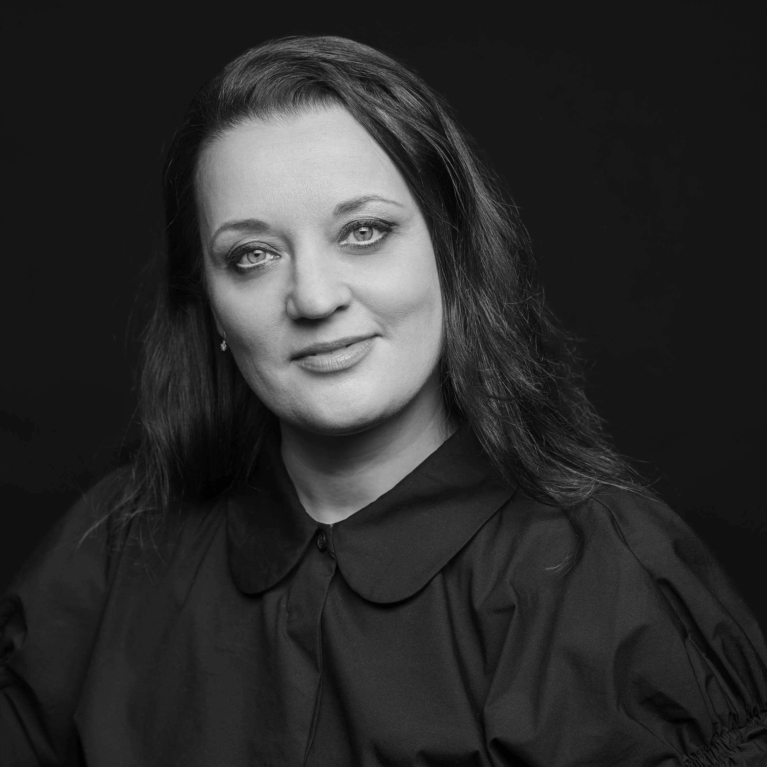 Une portrait noir et blanc d'une femme avec des cheveux longs et ondulés, portant une tenue sombre, contre un fond noir.