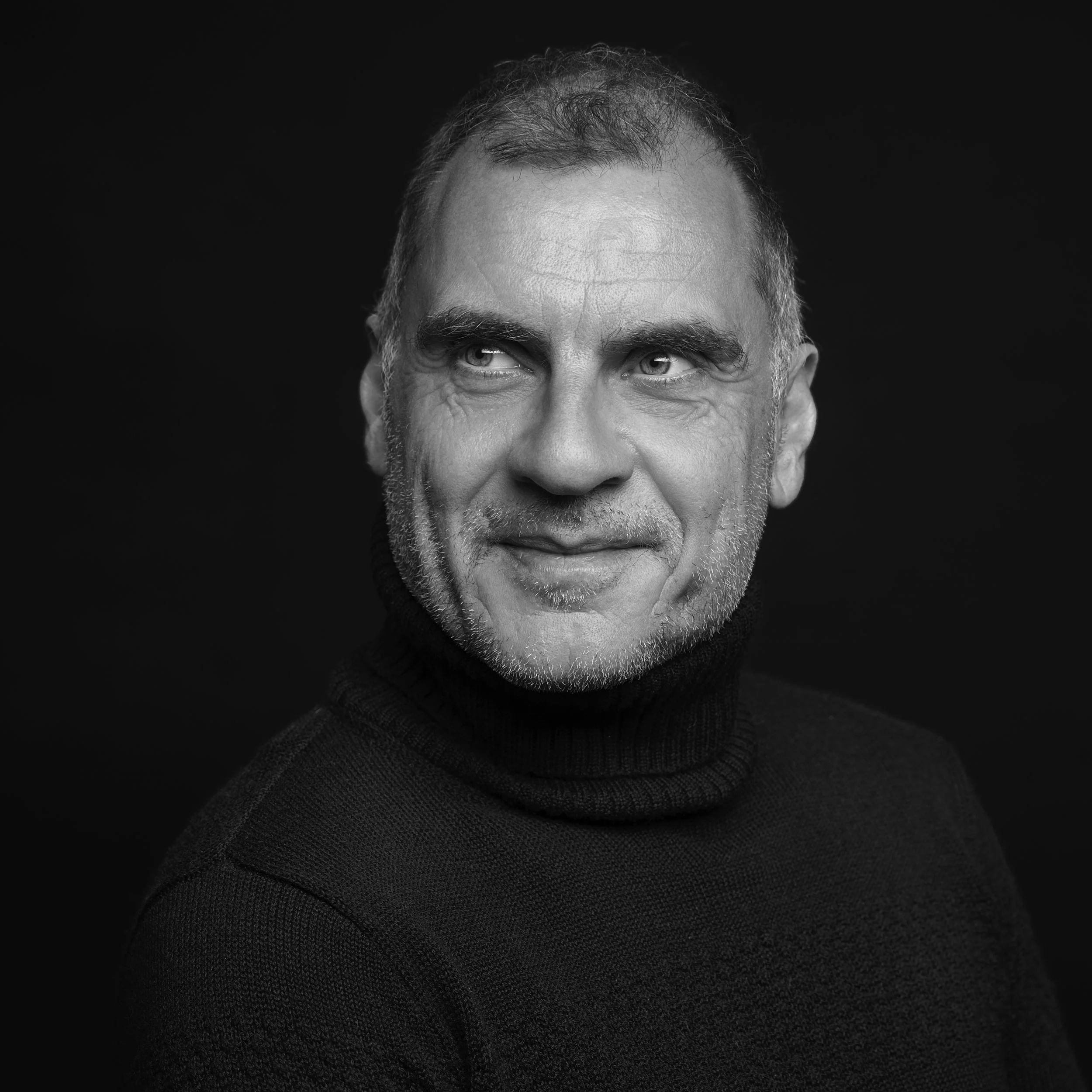 Portrait noir et blanc d'un homme avec des vêtements sombres, regardant vers la gauche, sur fond noir.